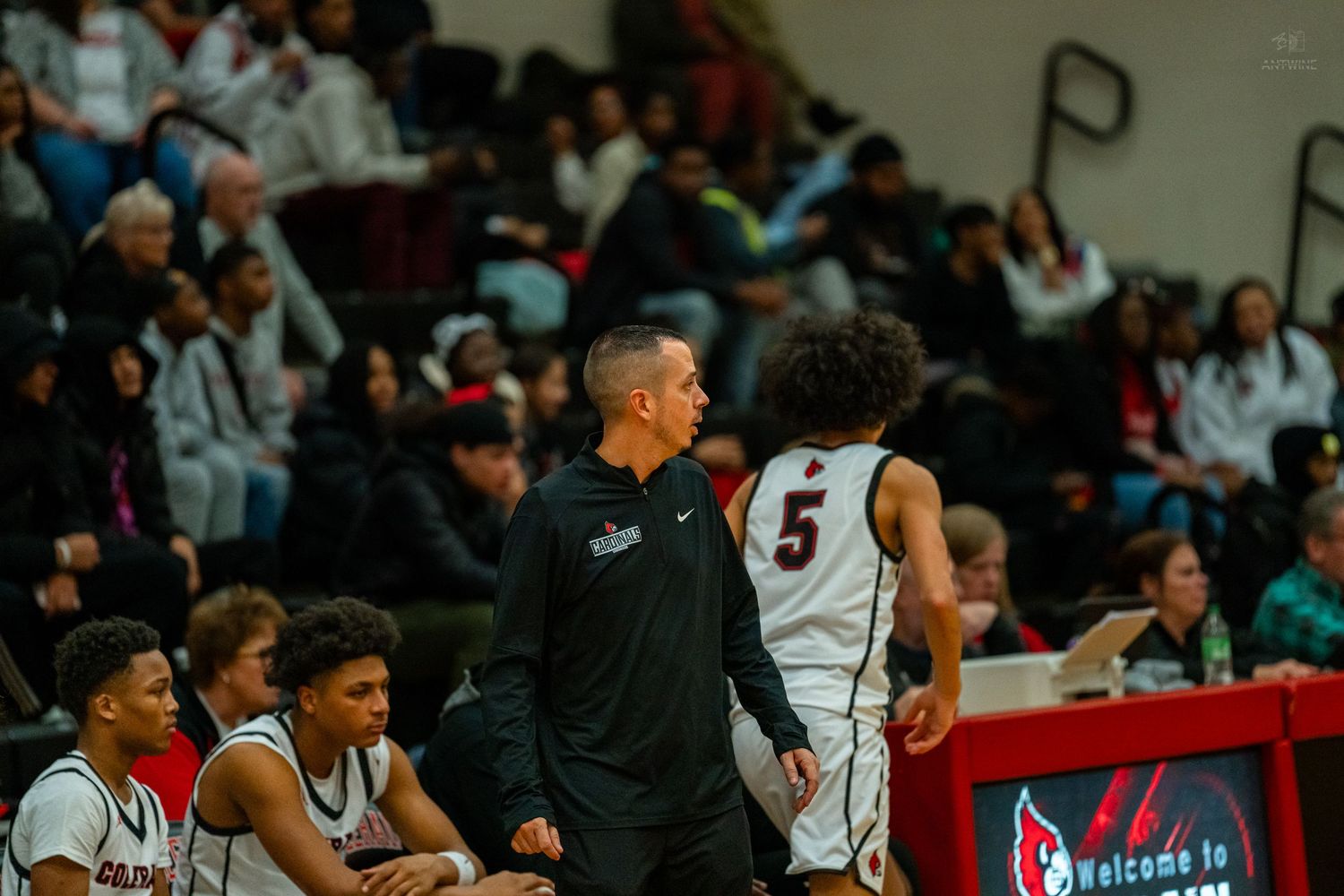 High school basketball coach talks with player #5 on the sideline during a game.