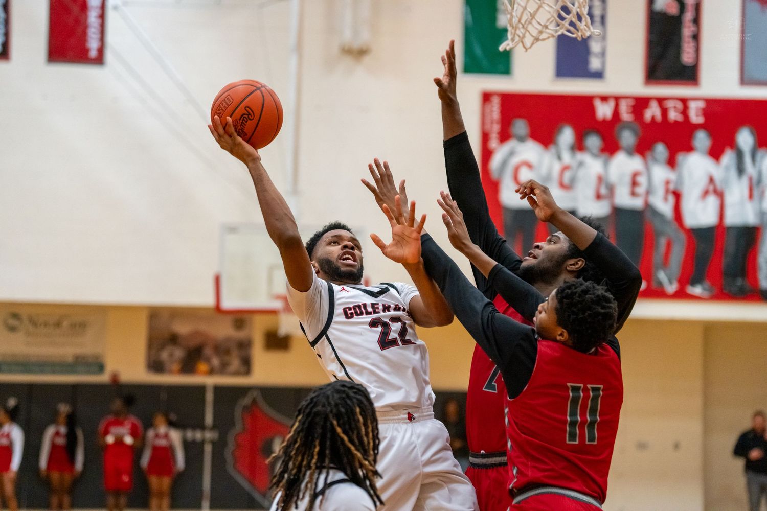A basketball player wearing number 22 attempts a layup against two defenders during a high school game.