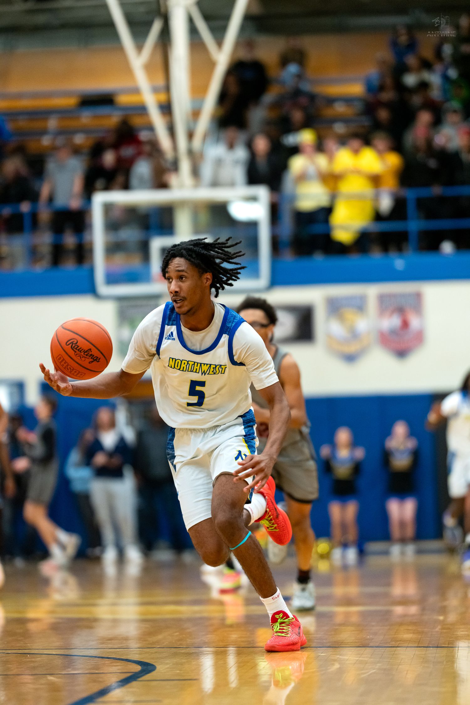 Northmen player #5 with dreadlocks dribbles ball upcourt during high school basketball game.