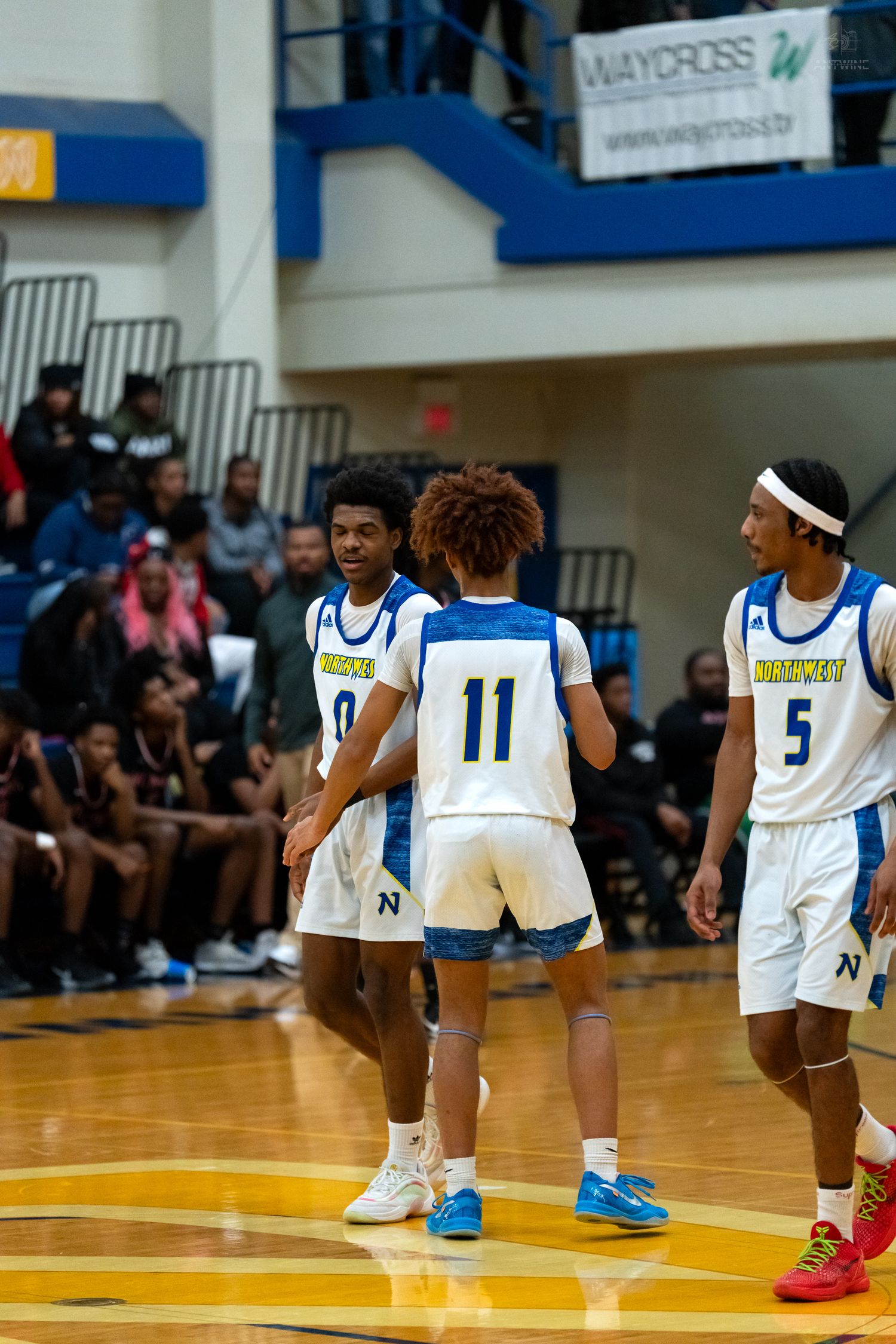 Three high school basketball players #0 #11 #5 in blue uniforms huddle during game.