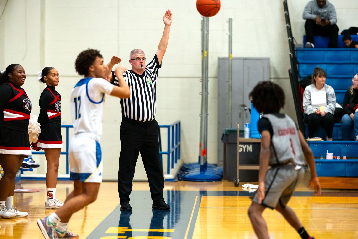 Referee signals a basket as players from two high school basketball teams compete on an indoor court.