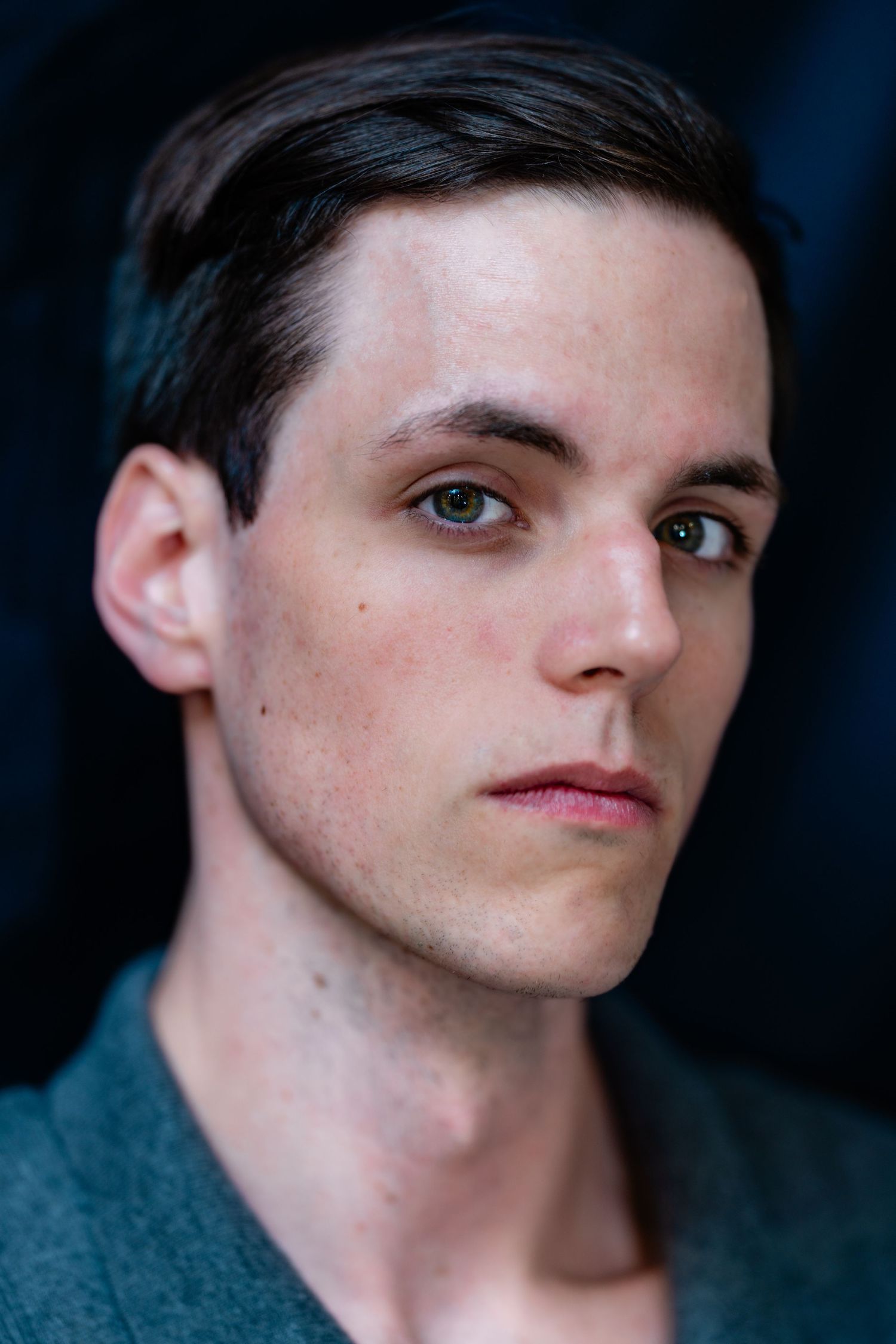 Close-up portrait of a young man with short dark hair and hazel eyes wearing a teal shirt.