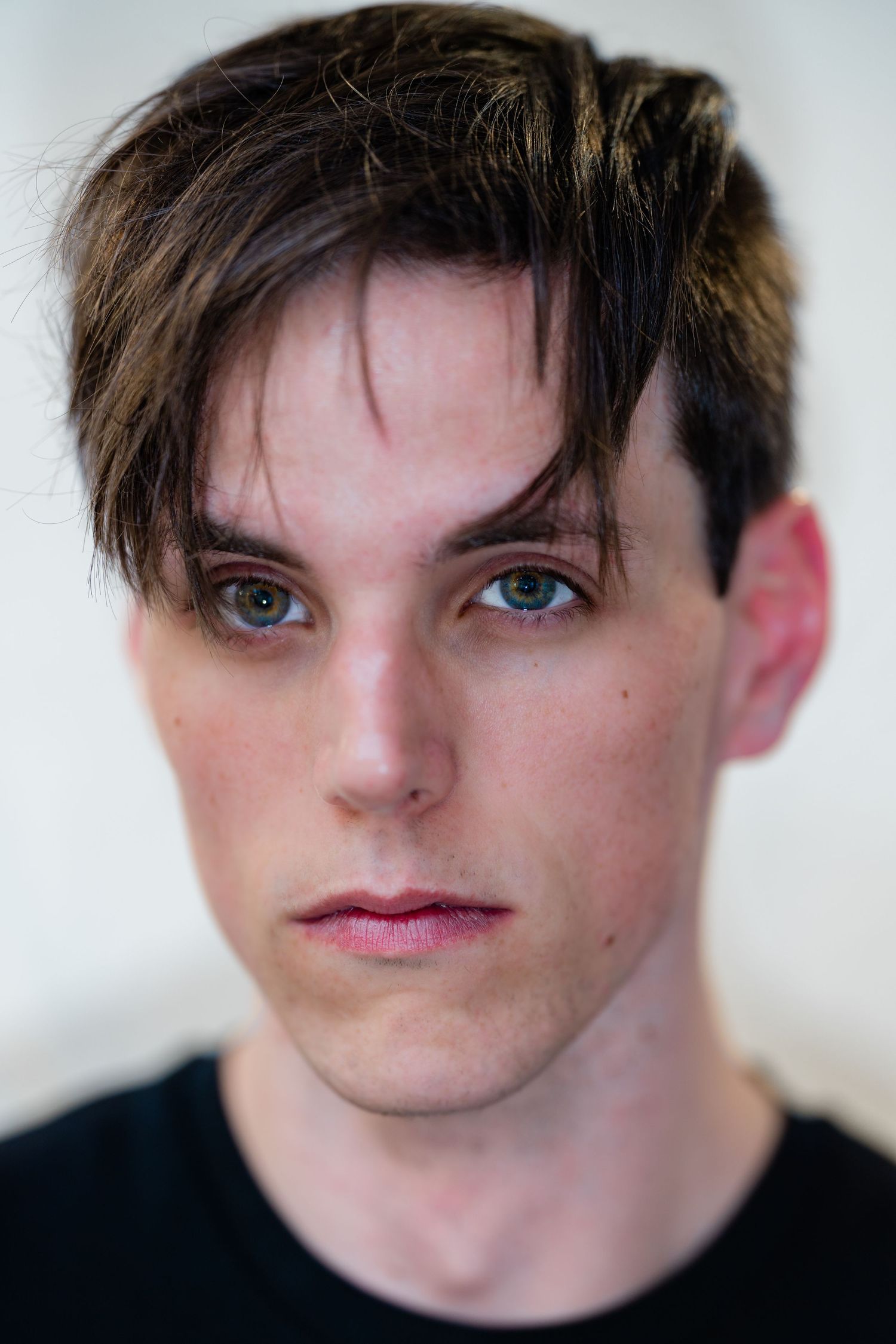 Close-up color portrait of a young man with dark swept hair and blue eyes in a black t-shirt.