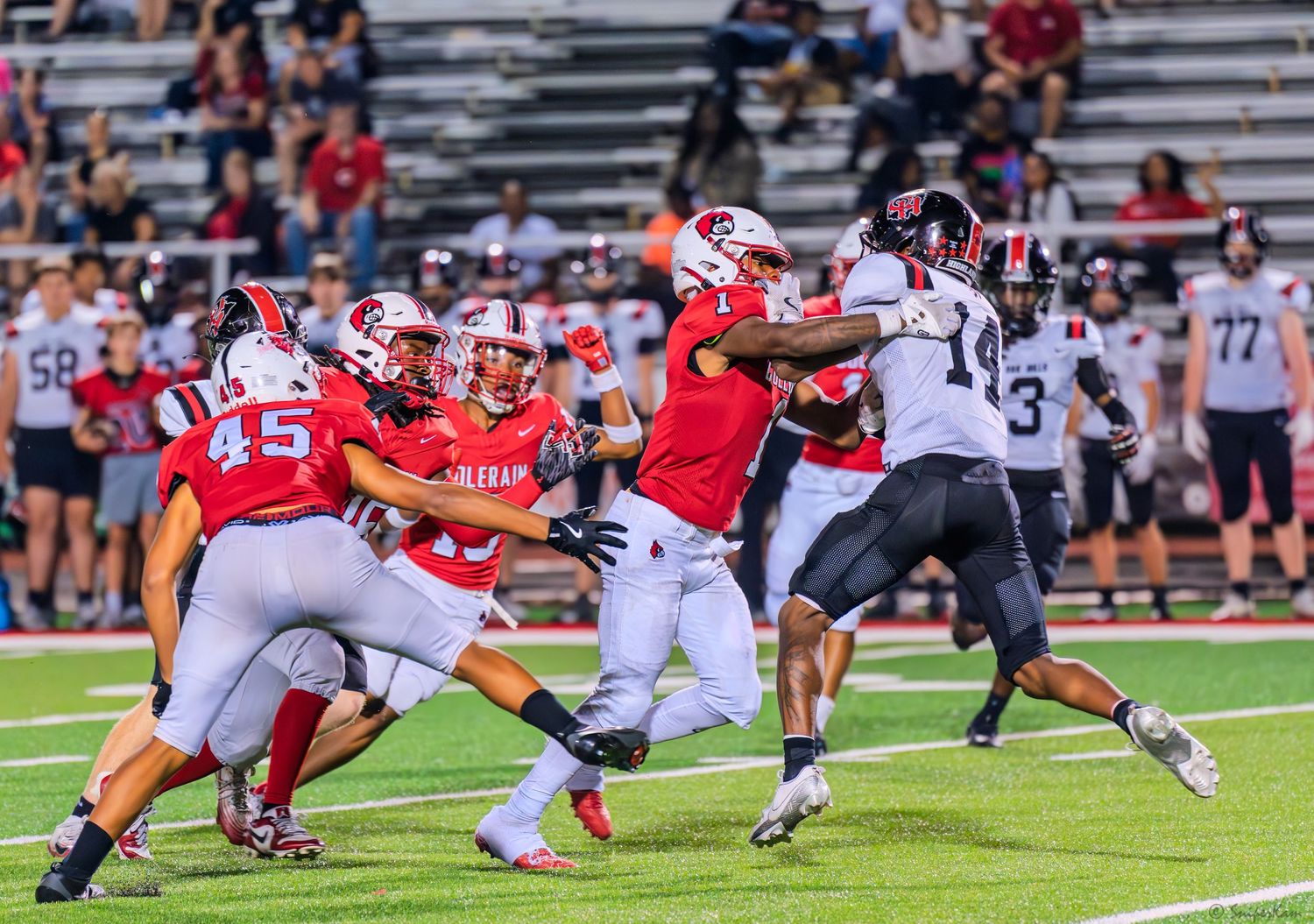 Colerain football players in red uniforms attempt to tackle a ball carrier during a night game.