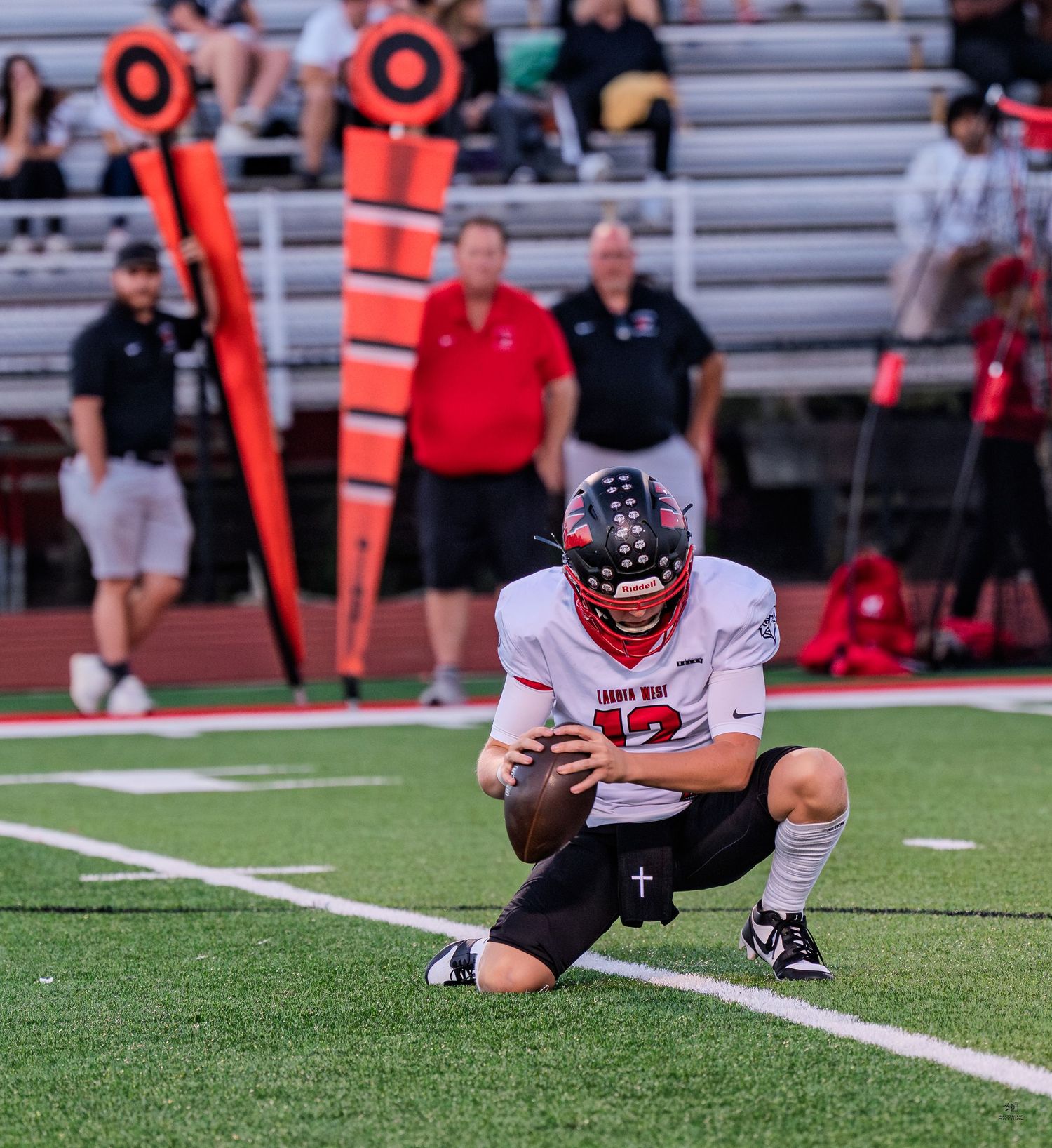 High school football player kneels on the field holding a football near the down marker during a game.