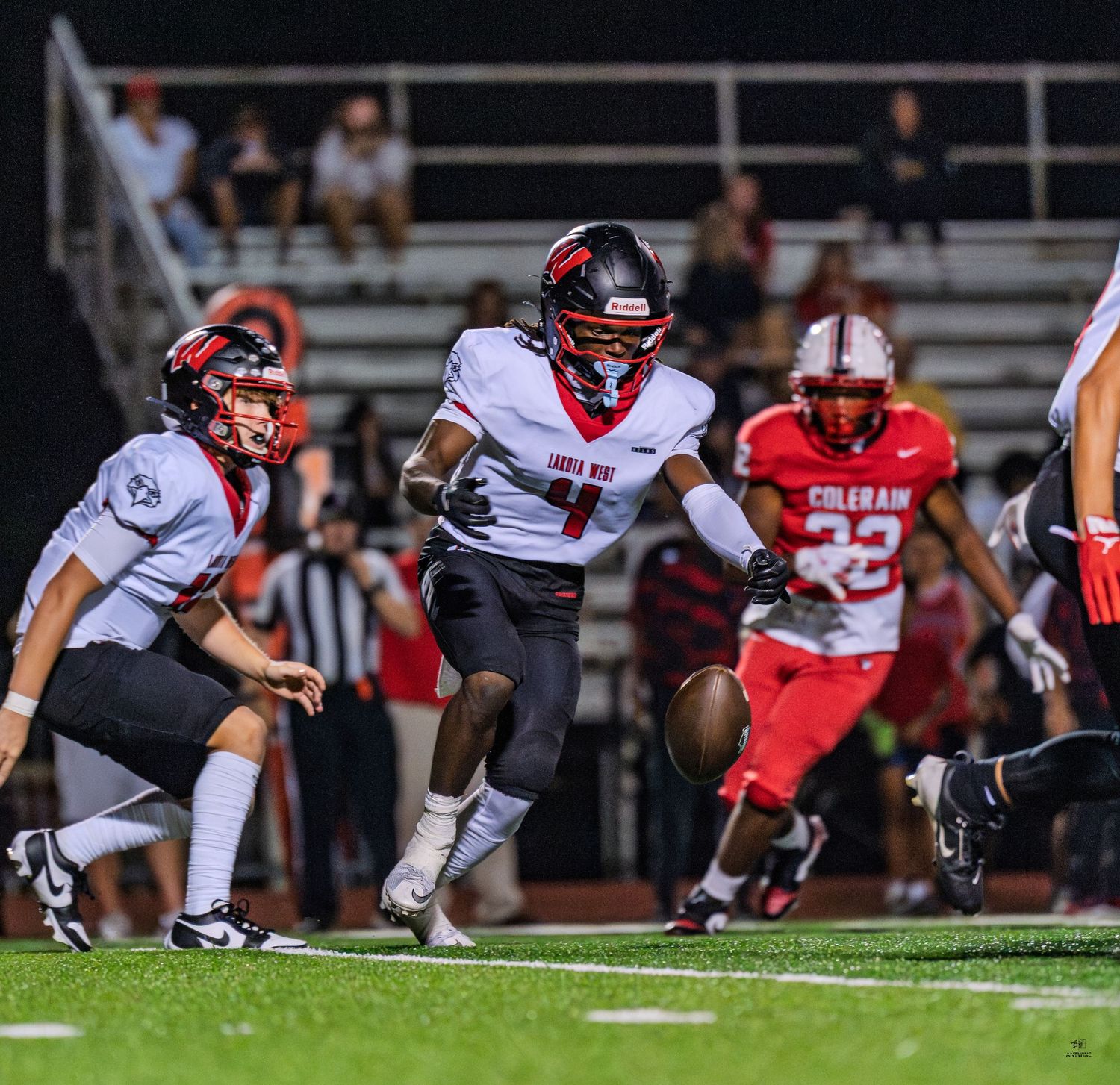High school football player carries ball past defenders during nighttime game on green turf field.