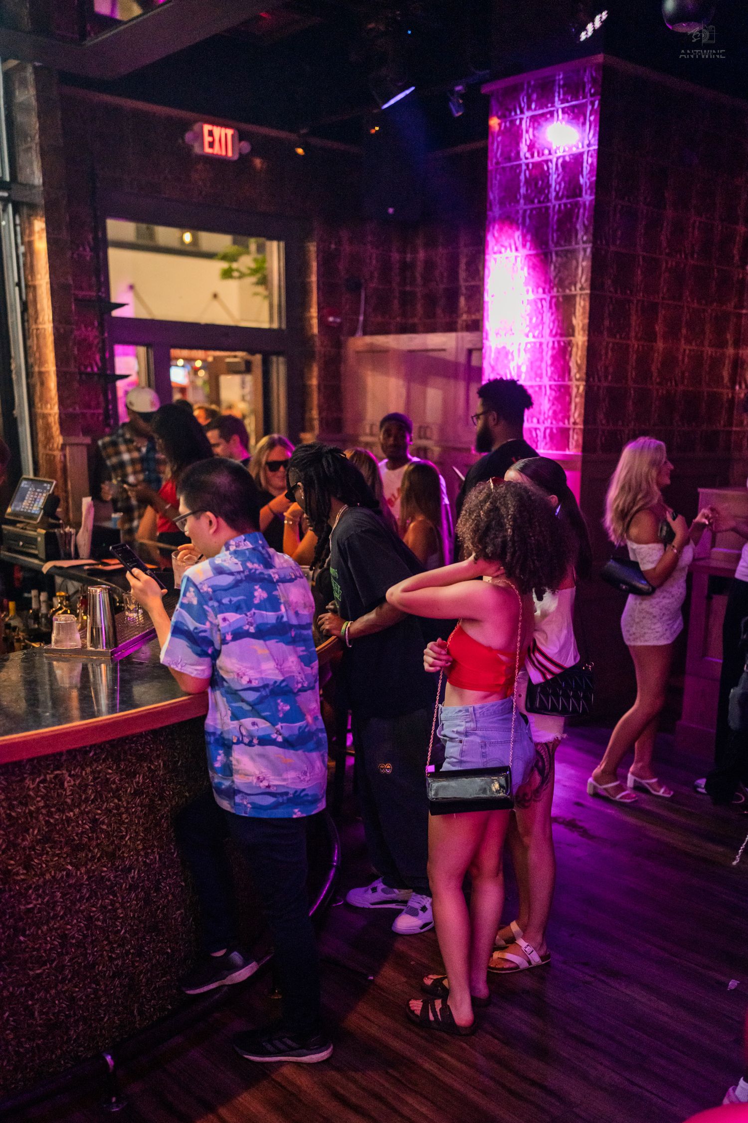 Guests mingle near a glowing pink bar column inside a lively nightclub venue.