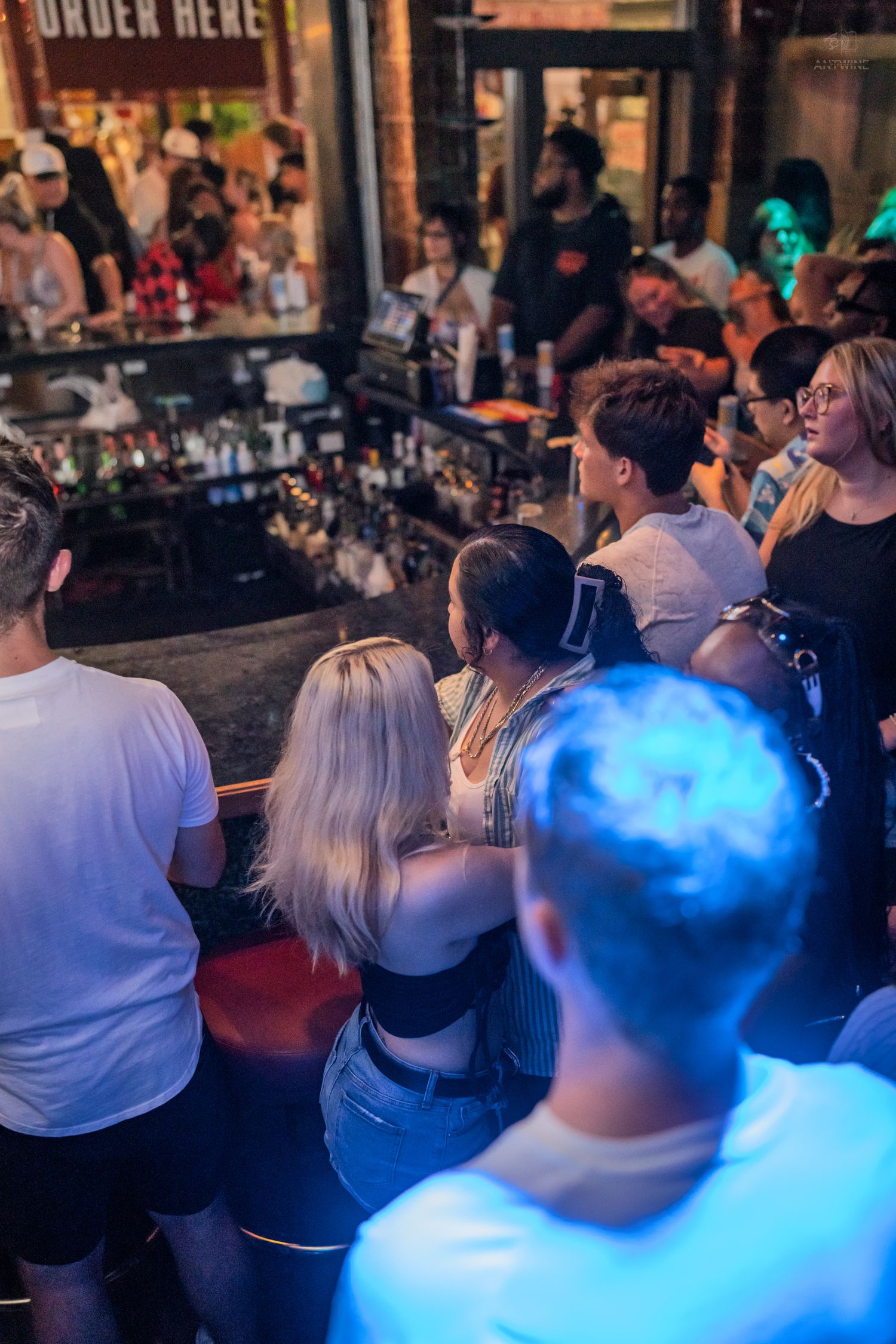 Bar patrons waiting to order drinks at a busy nightclub counter.
