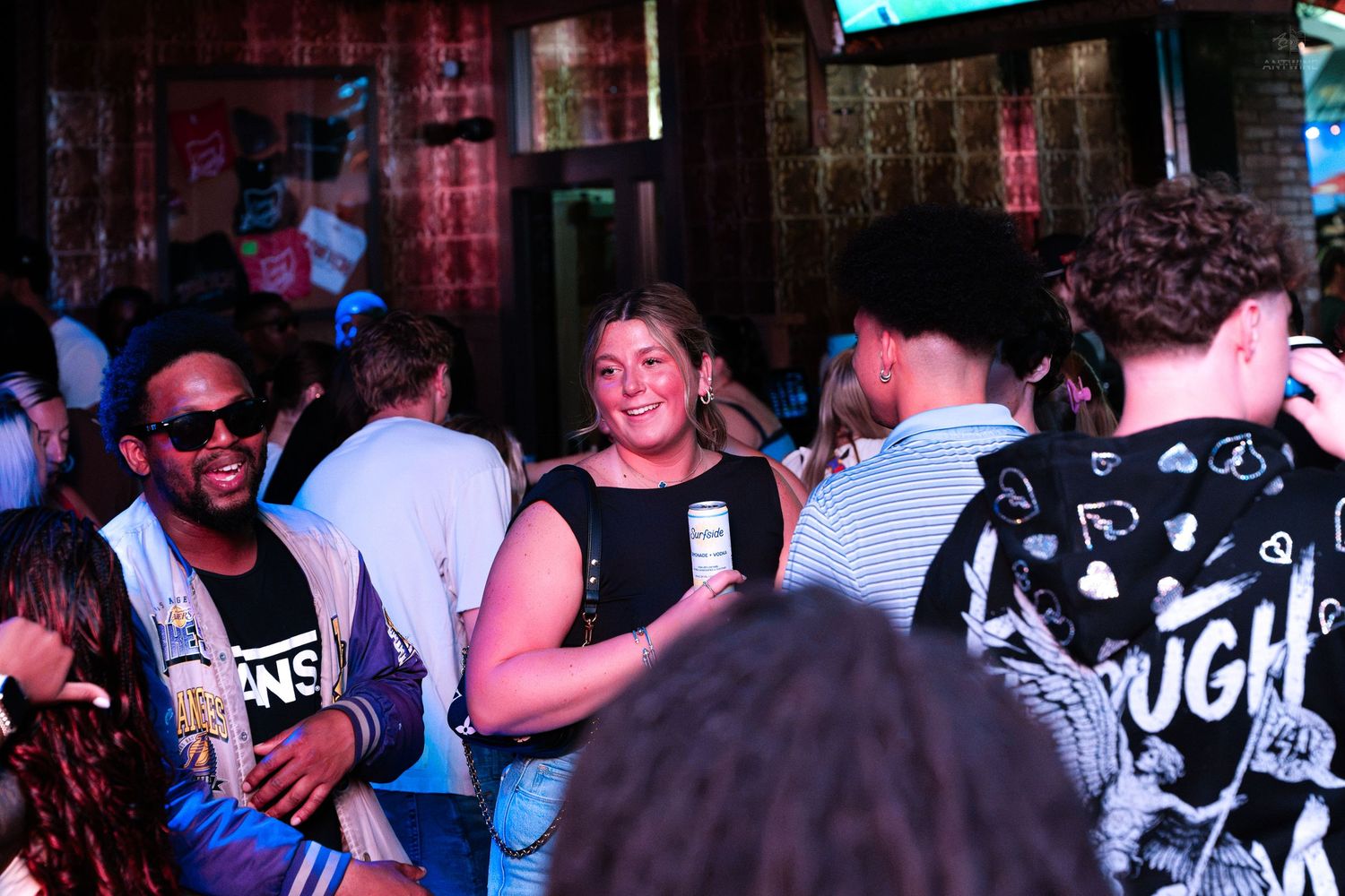 Diverse group of guests mingling and smiling at a crowded indoor bar or nightlife social event.