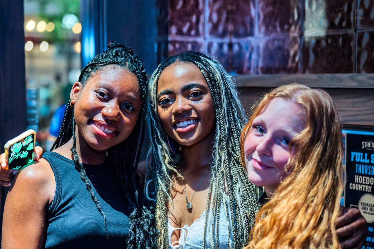 Three smiling women posing together inside a bar or nightclub venue.