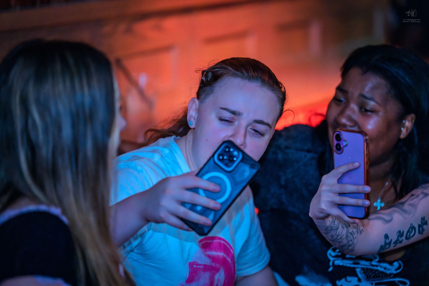 Young women taking selfies together with smartphones at a nightclub party.