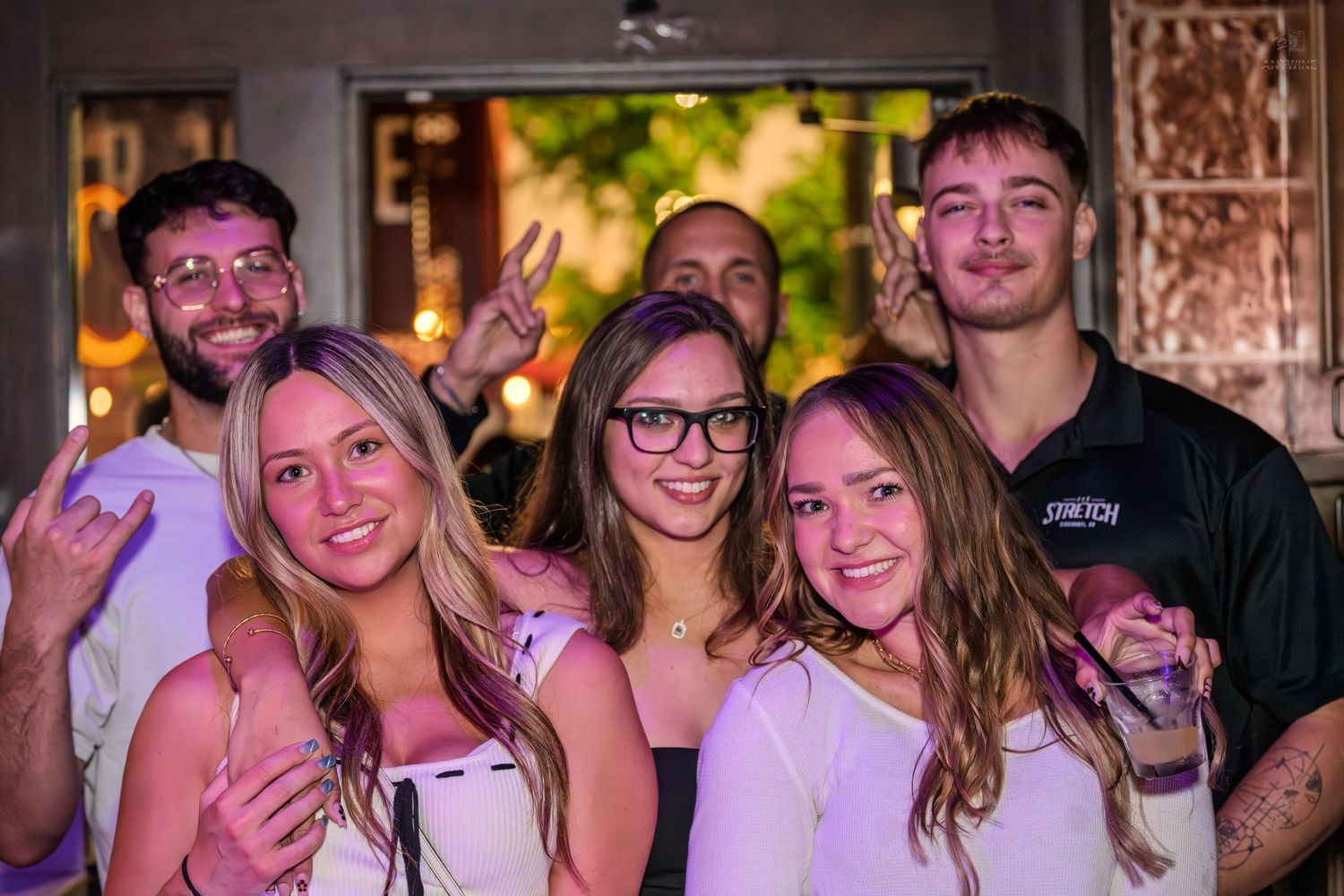 Group of young friends smiling and posing together outside a bar at night.