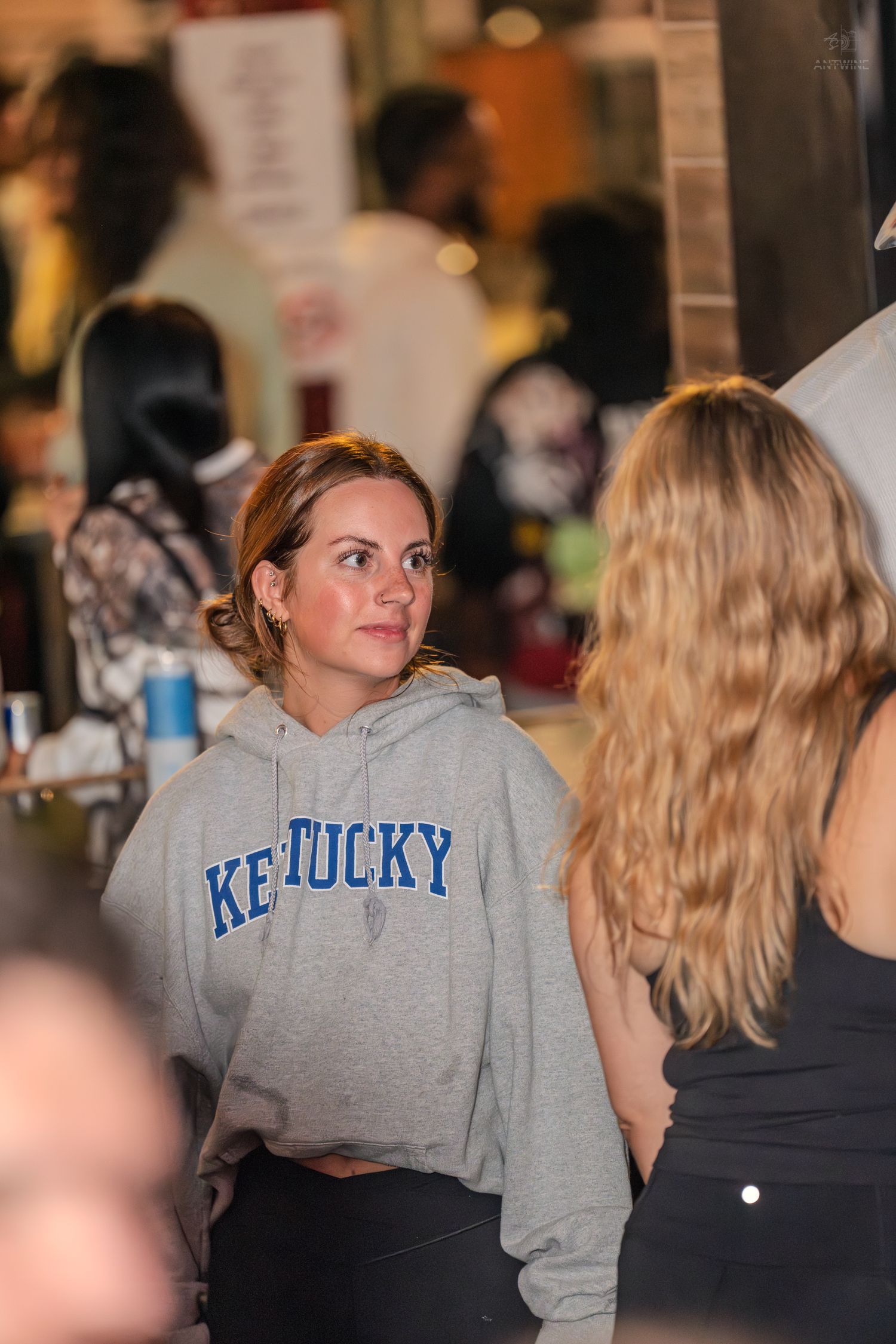 Woman in Kentucky hoodie at a crowded indoor event.