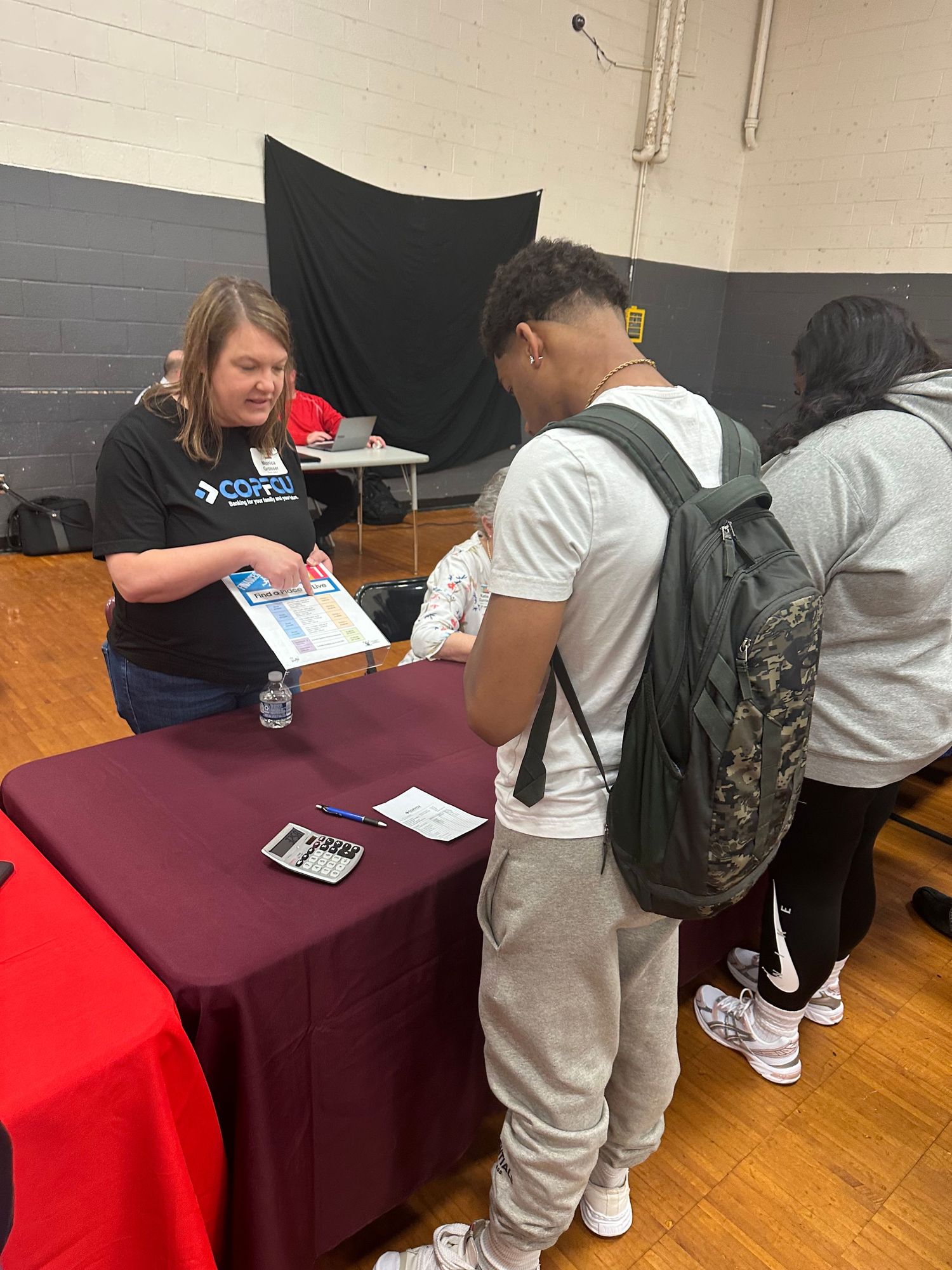 A student reviews materials at a maroon-draped table at an indoor school career fair event.