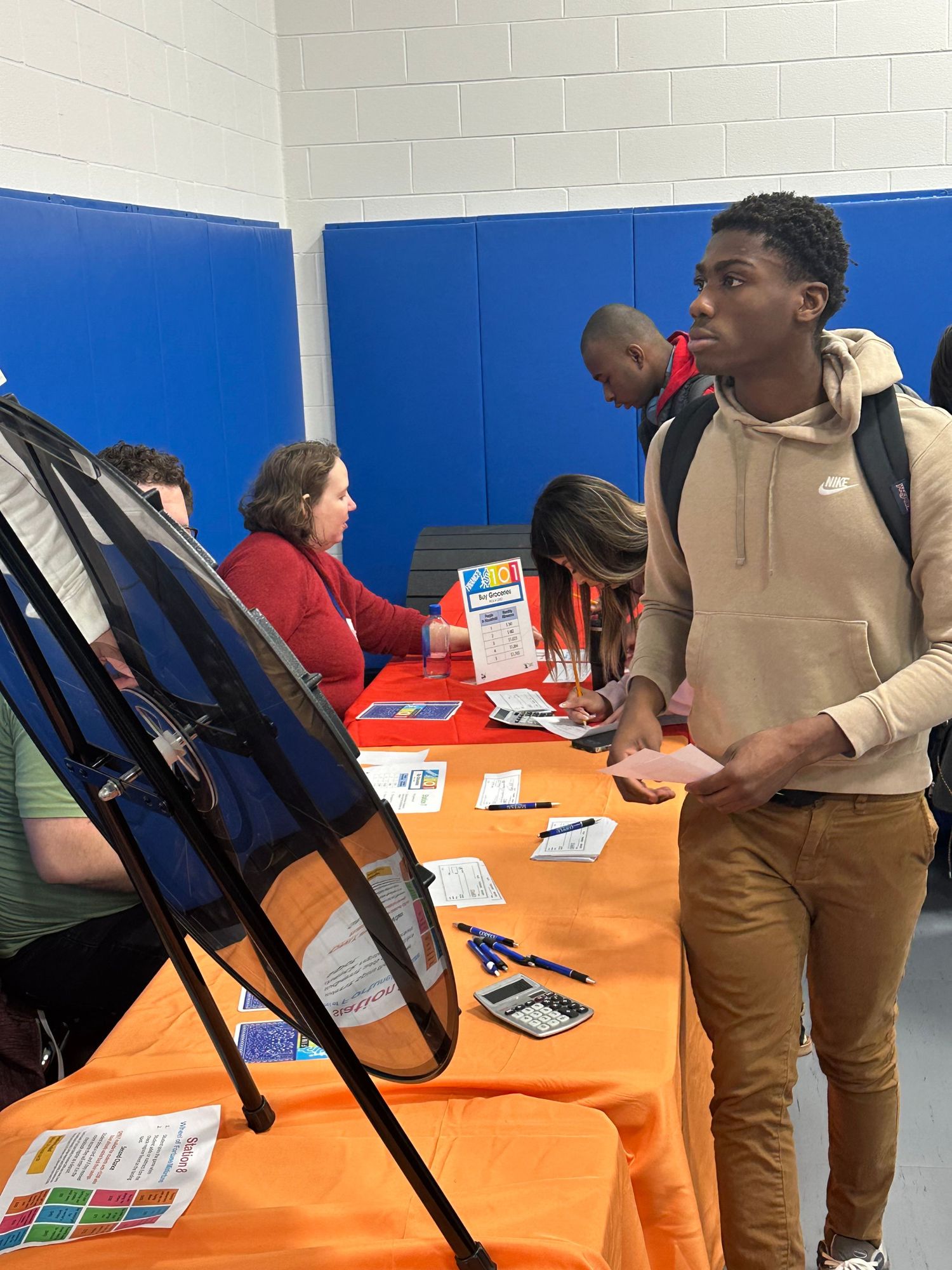 A student in a beige Nike hoodie browses an informational booth at a school fair event.