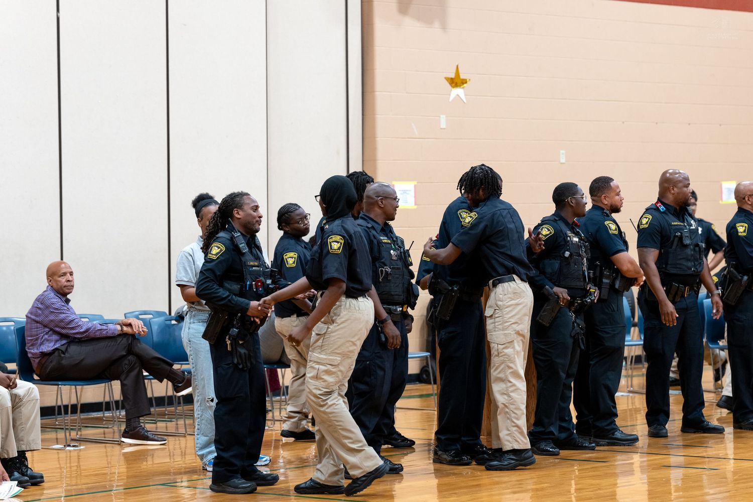 Law enforcement officers in uniform line up inside a gymnasium during an official ceremony or training event.