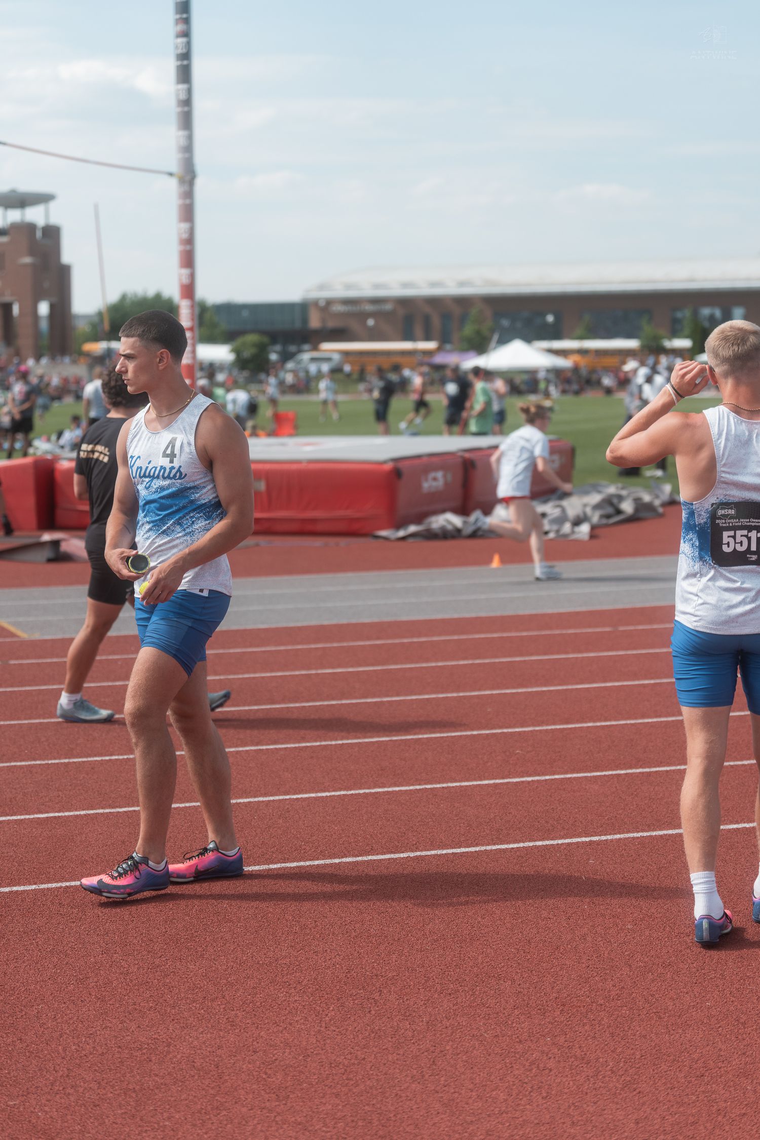 Two Knights relay runners exchange baton on red track at outdoor high school track competition.