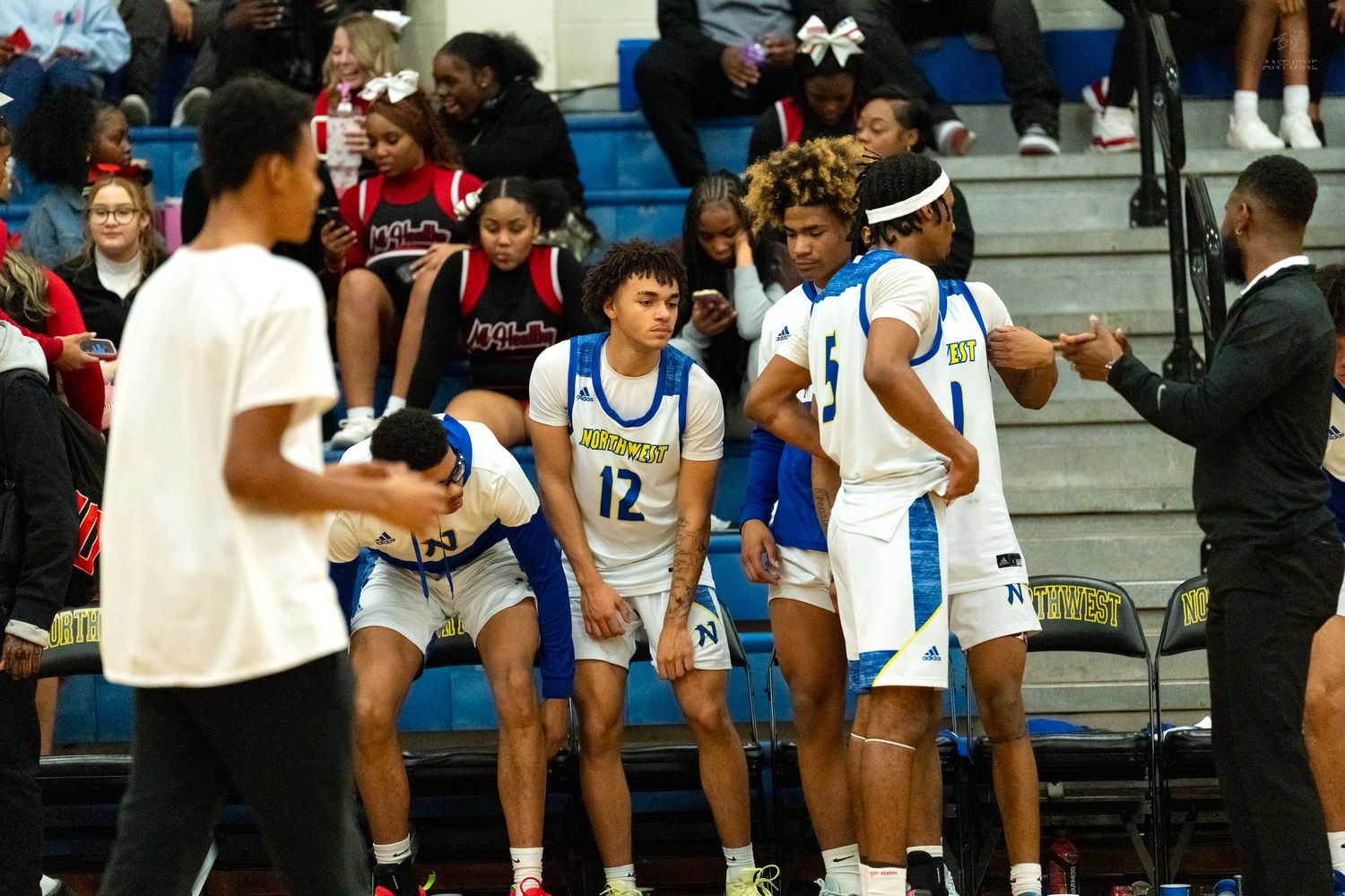 High school basketball players in blue and red uniforms huddle together during a break in an indoor game.