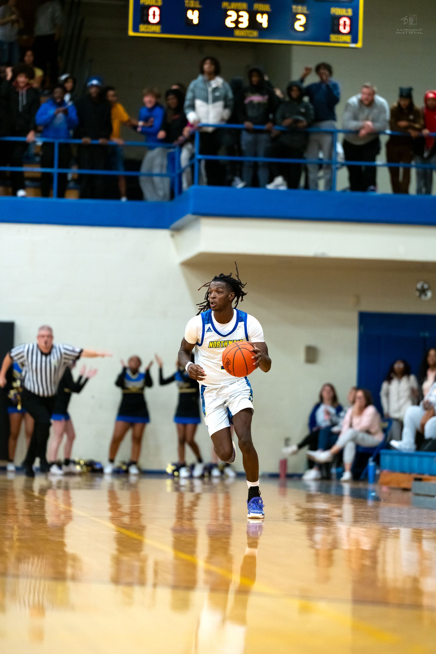 A basketball player in a blue and white uniform dribbles down the court during a game.