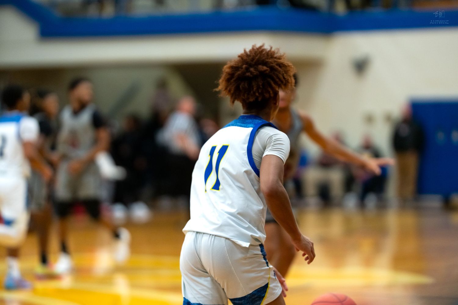 High school basketball player wearing number 11 white uniform runs down court during an indoor game.