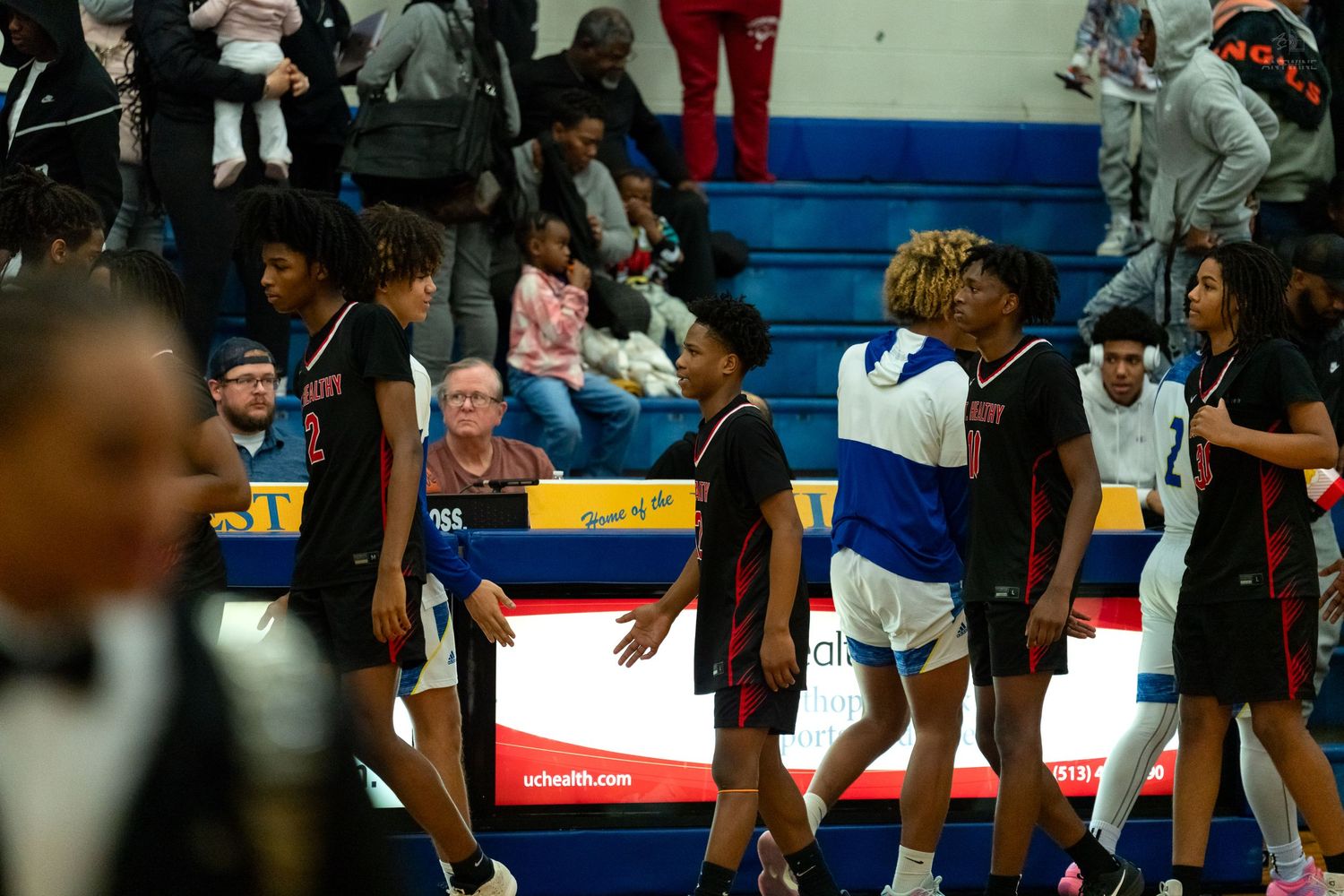 Northwest Knights and opposing team players shake hands on court following a high school basketball game in a gymnasium.