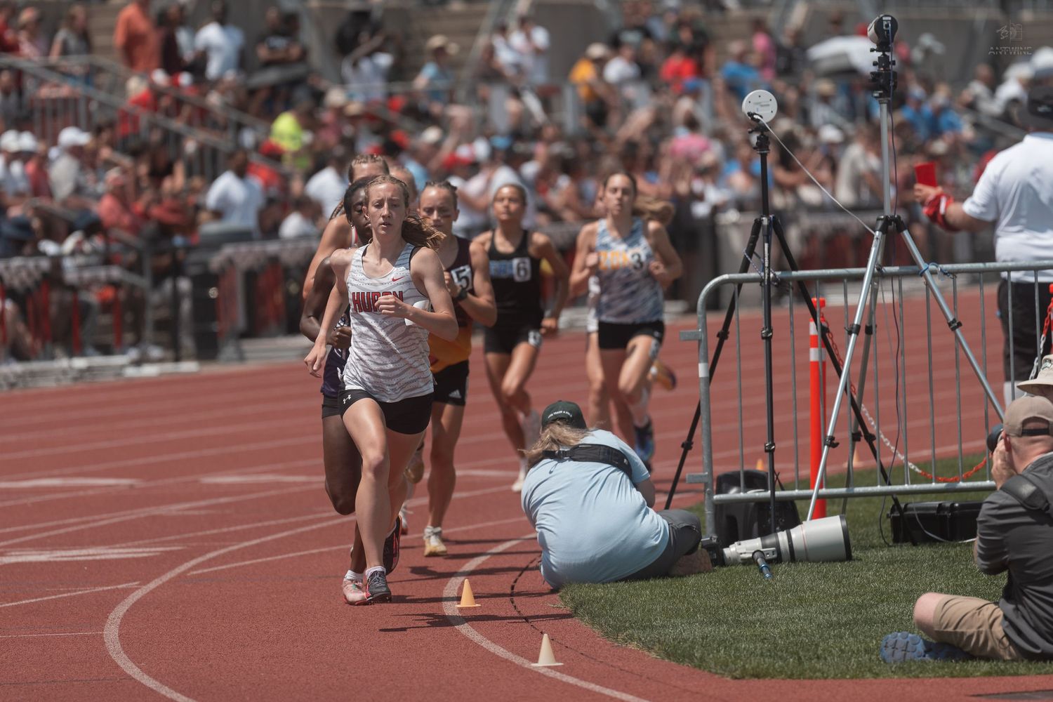 Female runners compete in a track race at an outdoor high school track and field meet on a sunny day.