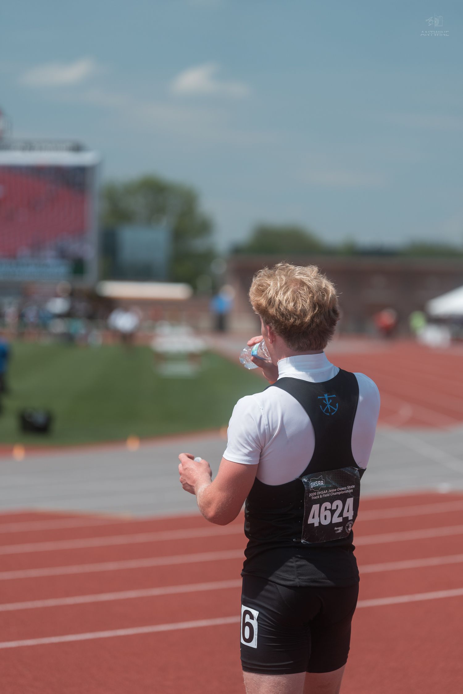 Athlete wearing bib number 4624 stands on red track at sunny outdoor competition.