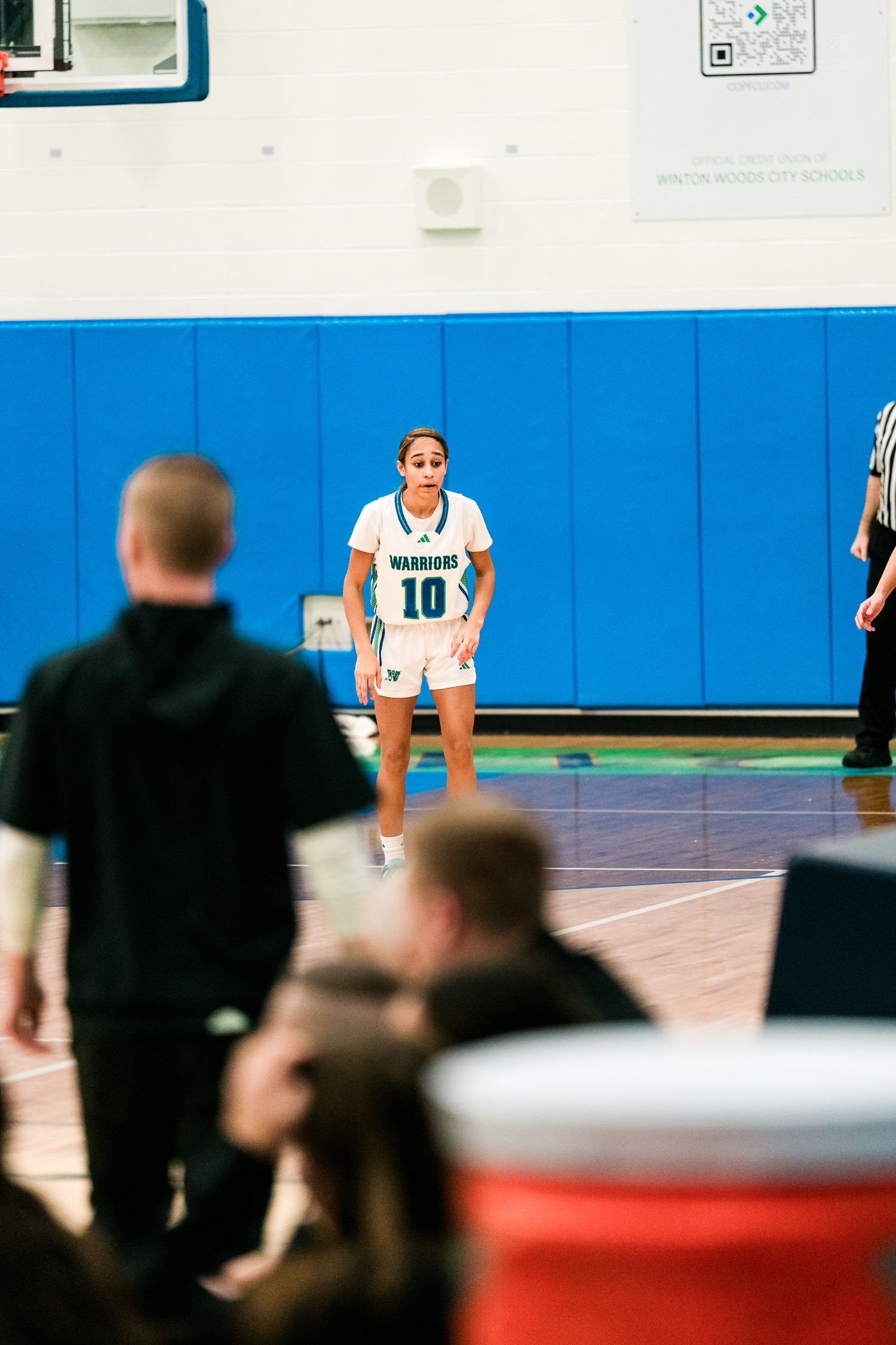 Warriors girls basketball player number 10 stands on the court during a stoppage in play at a high school game.