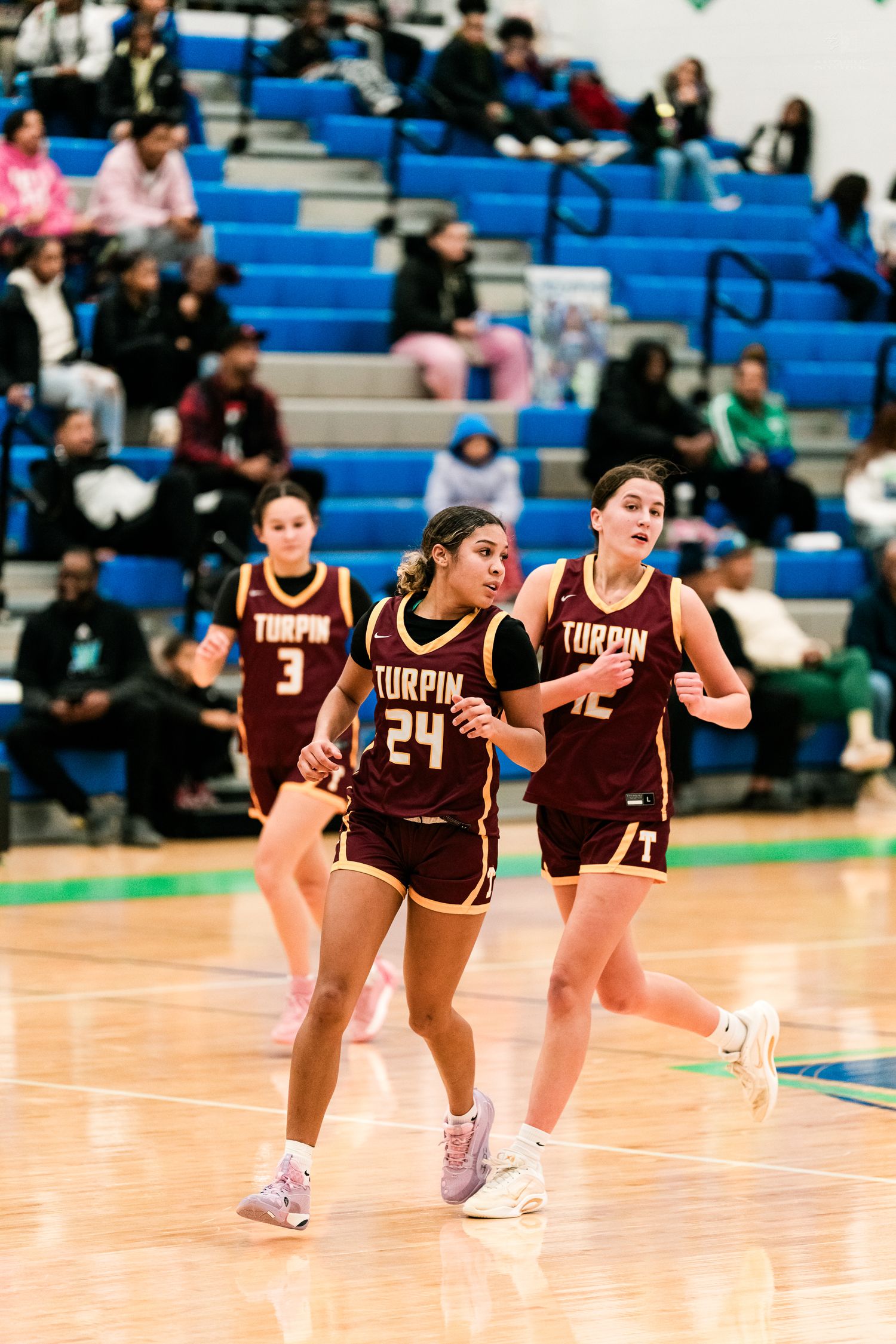 Two Turpin high school girls basketball players in maroon uniforms run during a game.