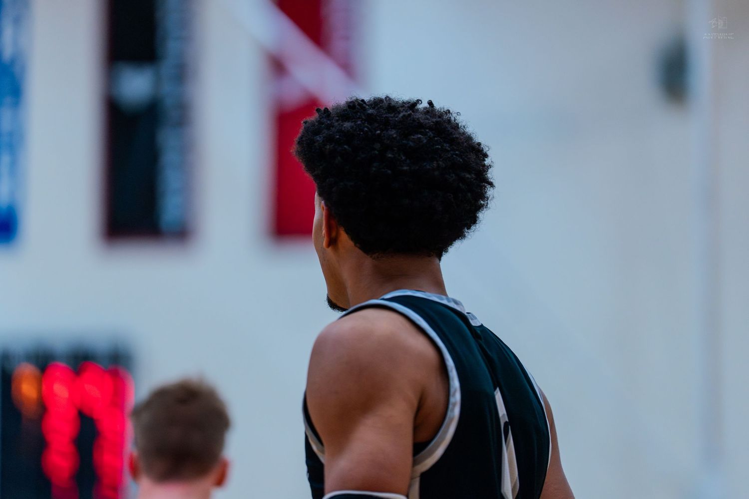 Close-up rear view of a curly-haired basketball player in a dark jersey during a game.