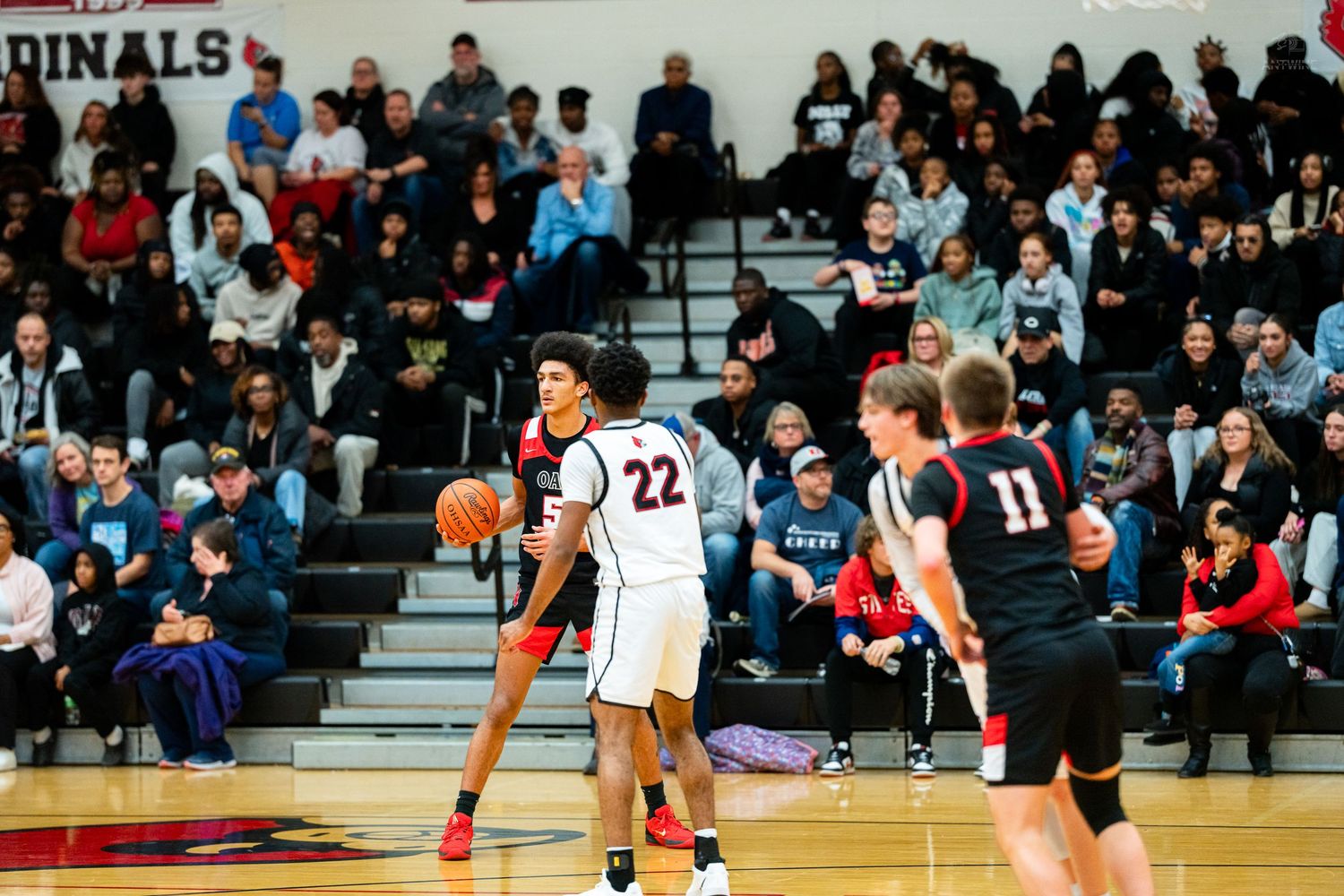High school basketball player number 22 dribbles ball while defender in red approaches during gym game.