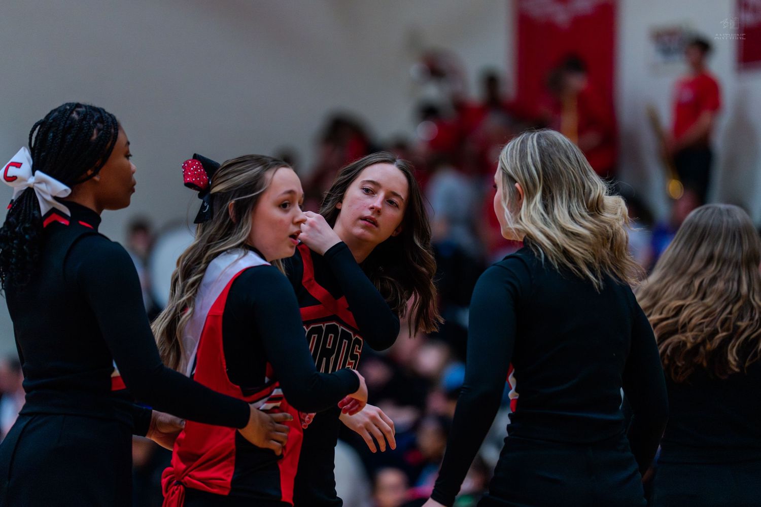 High school cheerleaders in red and black uniforms huddle together during a basketball game.