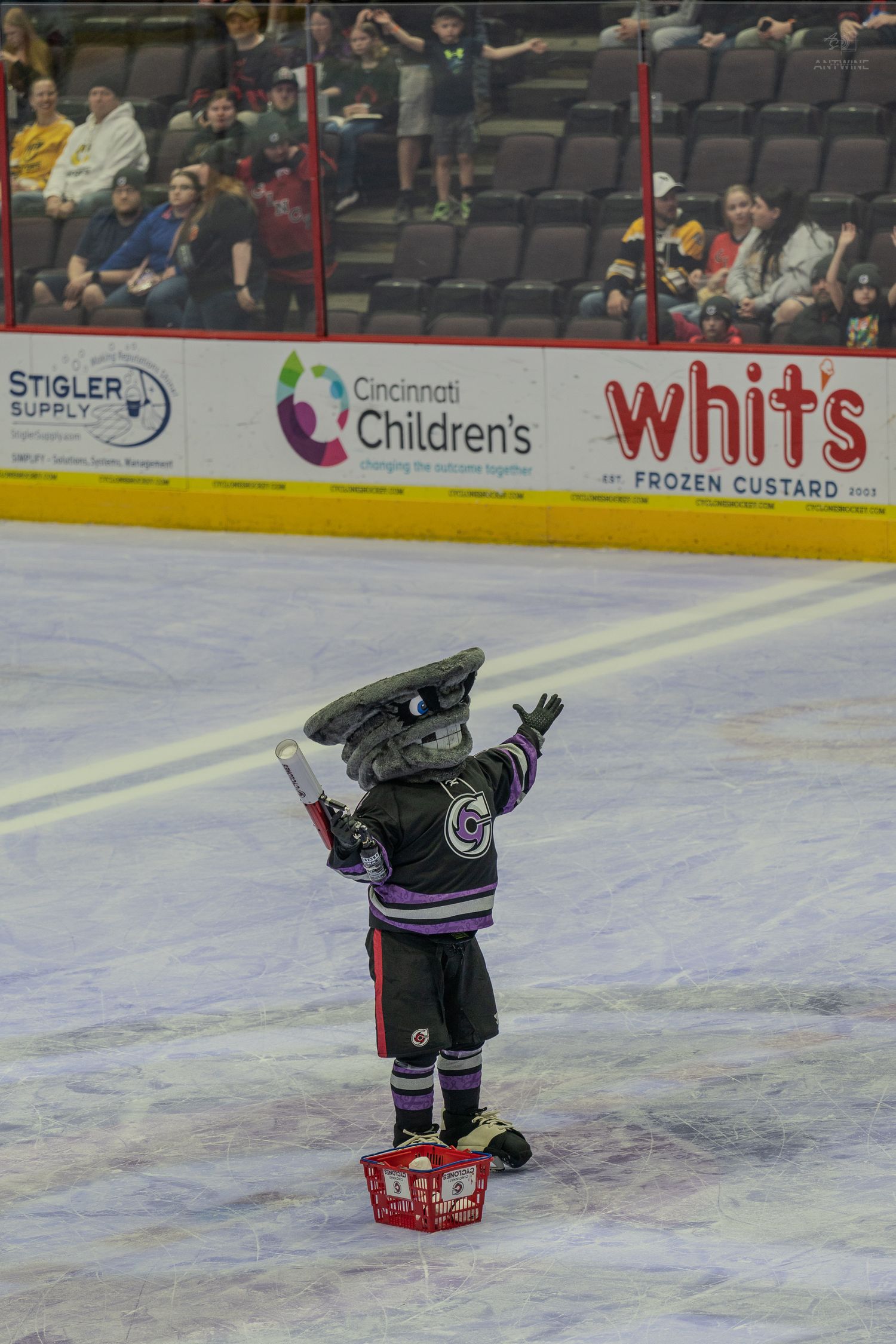 Cincinnati Cyclones hockey mascot raising hands on ice rink during arena game.