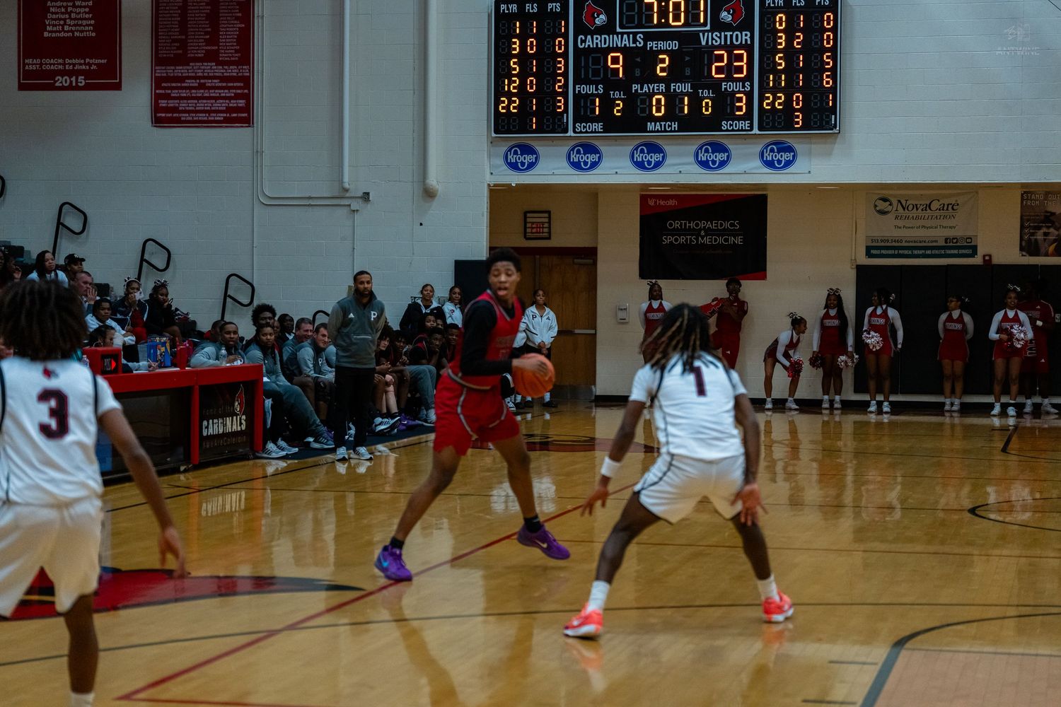 High school basketball player in red dribbles against defender during Cardinals home game.