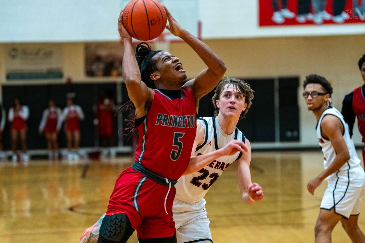 Princeton player #5 drives to basket for layup against defender #23 in competitive high school basketball game.