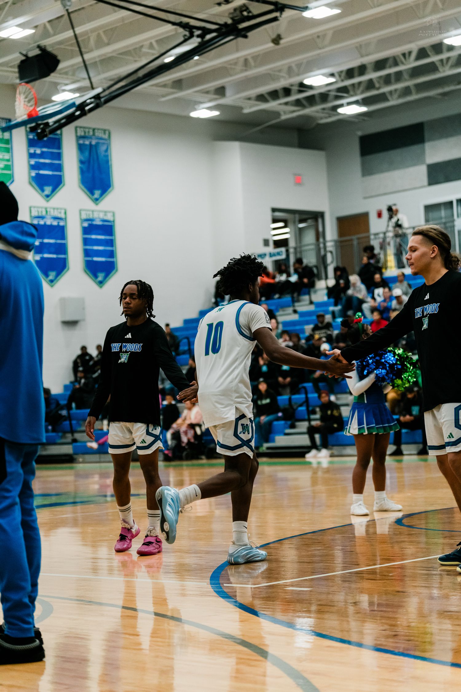 Basketball player #10 in white uniform runs through player introductions at high school gymnasium.