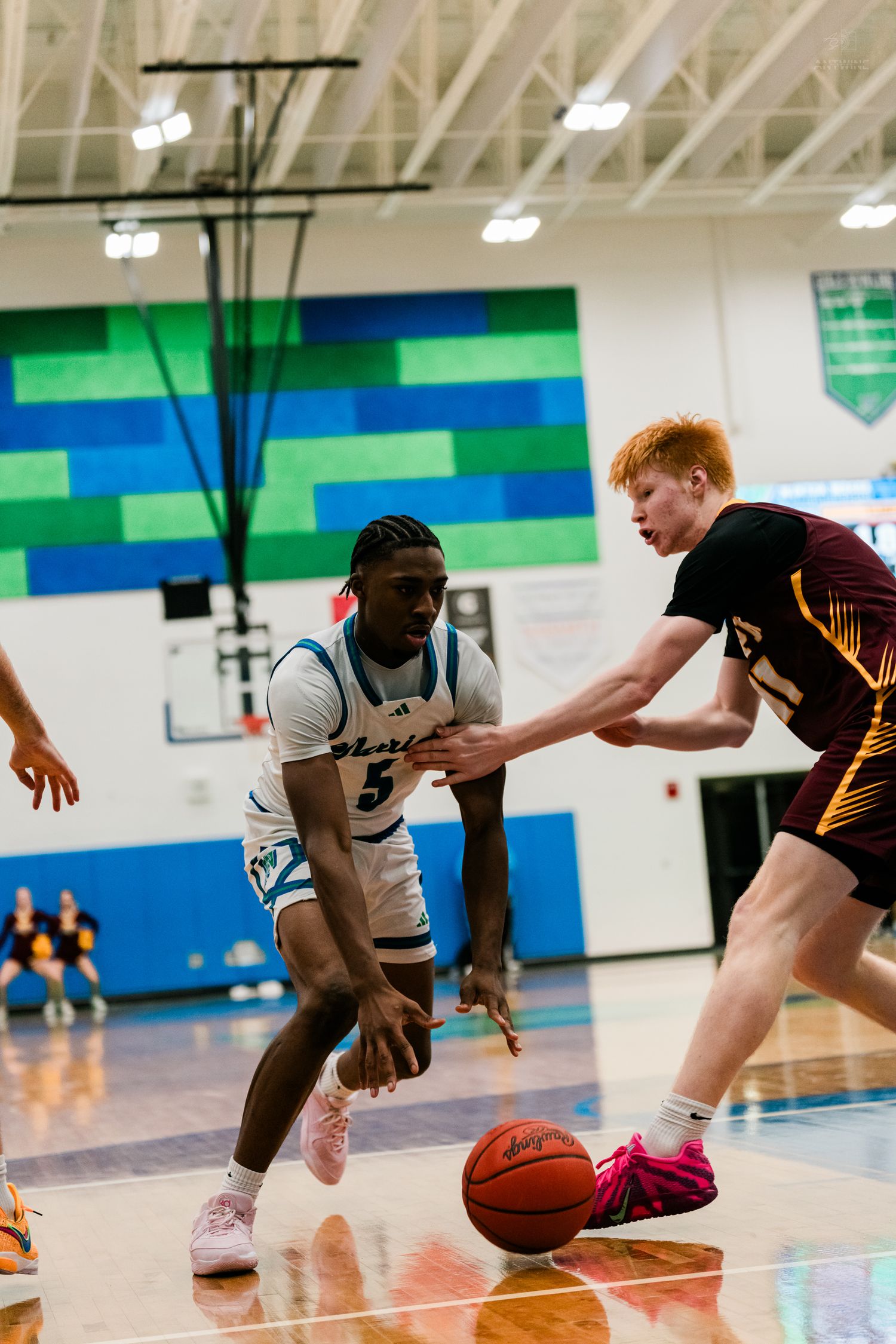 Player #5 in white Warriors jersey dribbles past a red-haired defender during a competitive high school basketball game.