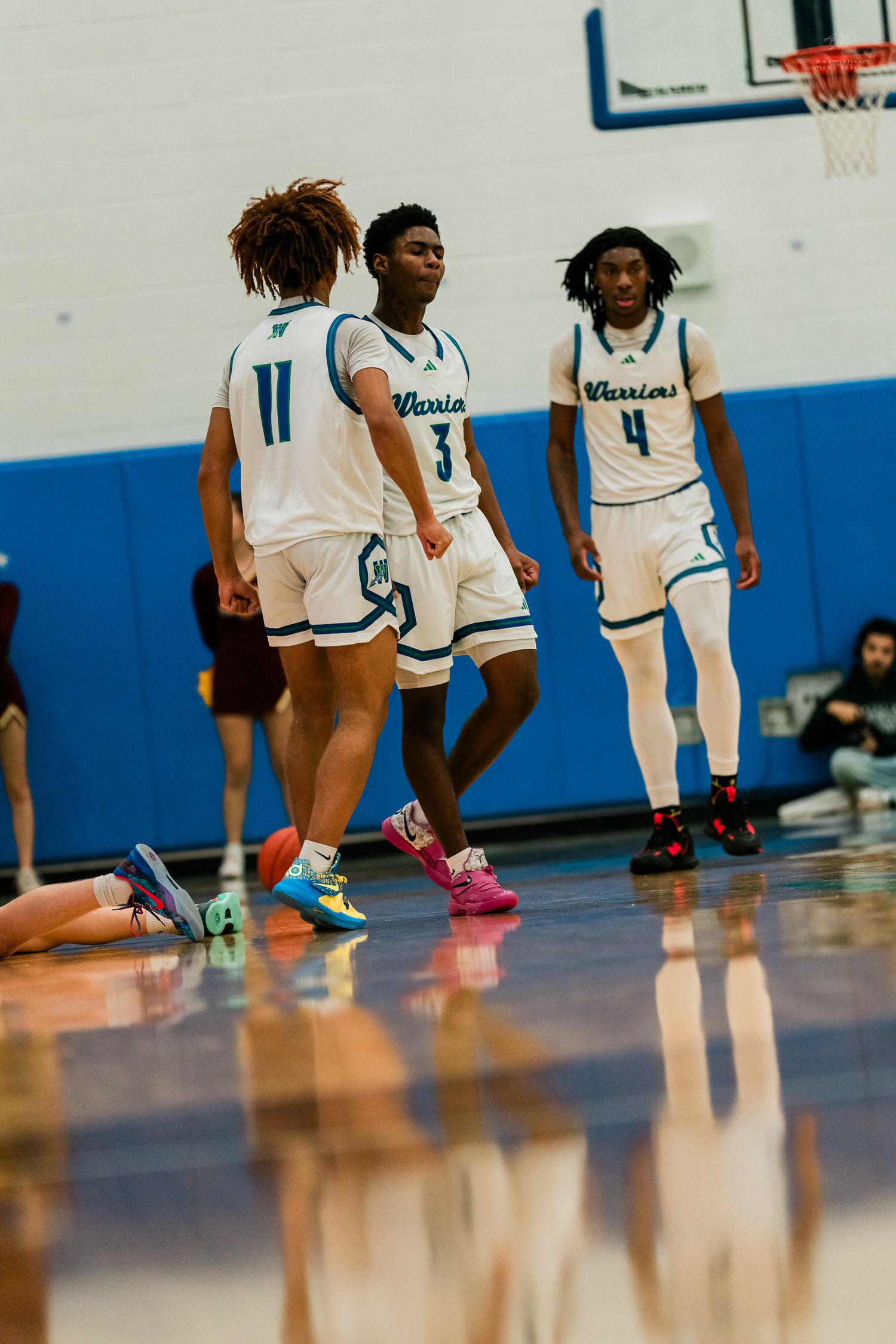 Three Xavier Warriors basketball players in white uniforms gather on the court during a high school game.