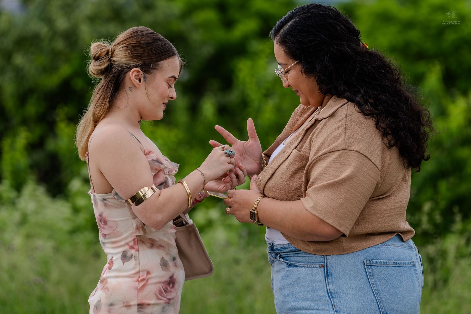 Two women examining a ring during an outdoor proposal in a green garden setting.