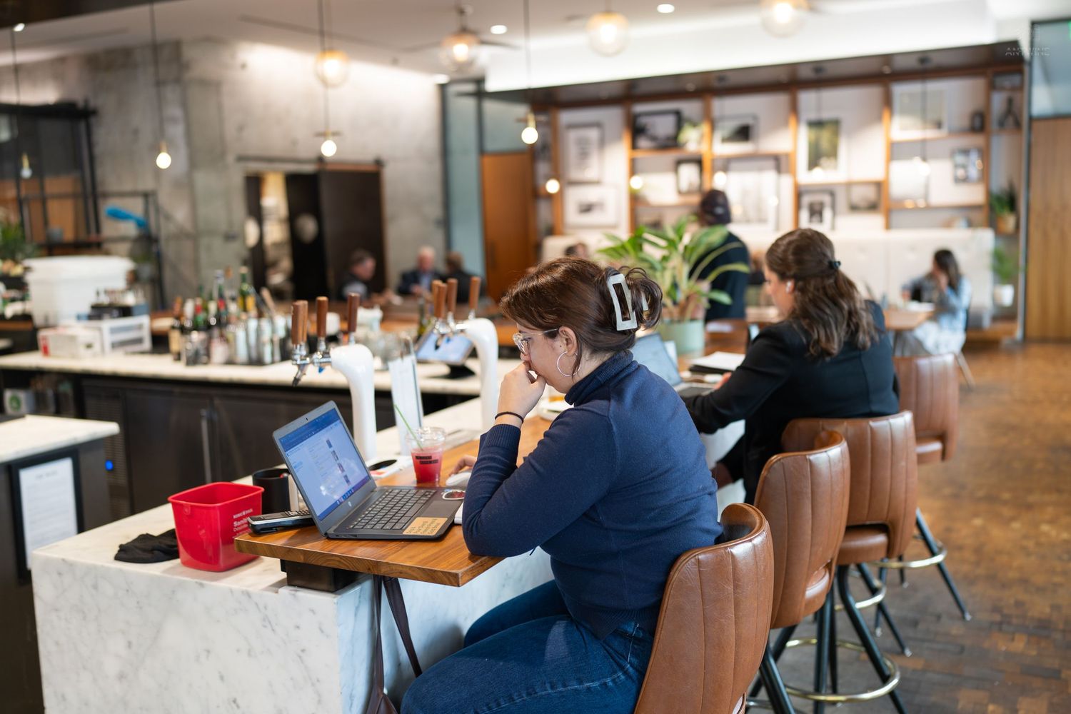Woman working on laptop at marble bar counter inside a modern cafe with warm ambient lighting.