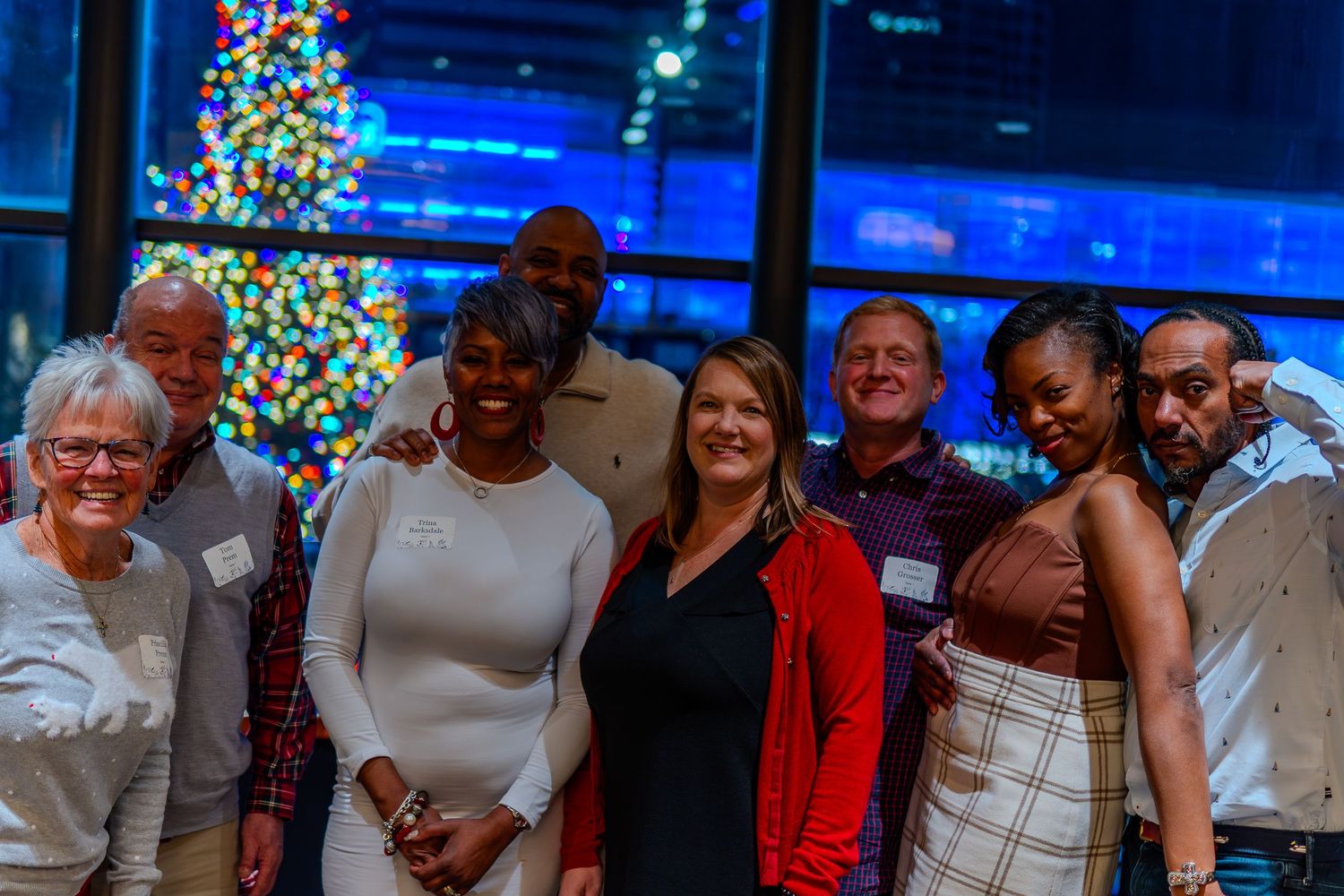 Group of diverse colleagues smiling together at a festive holiday office party with a decorated Christmas tree in the background.