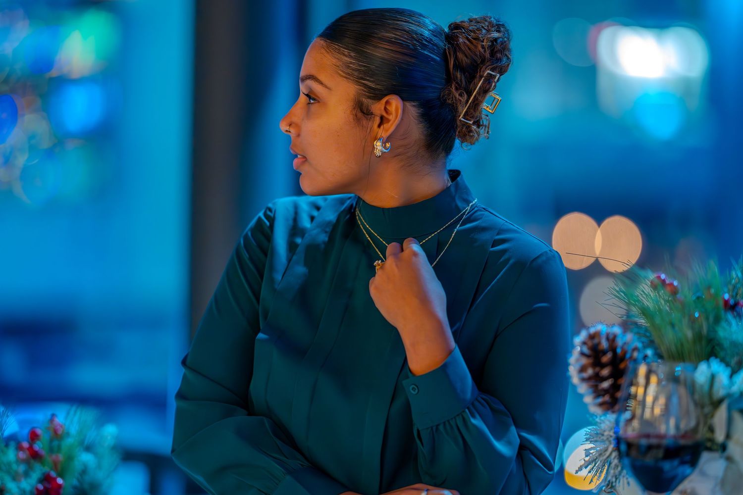 Elegant woman in teal turtleneck dress at festive holiday event with blue ambient lighting and pine cone decor.