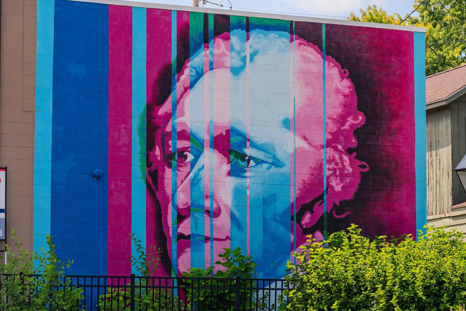 Colorful mural of a historical figure painted in pink and blue stripes on a building exterior.