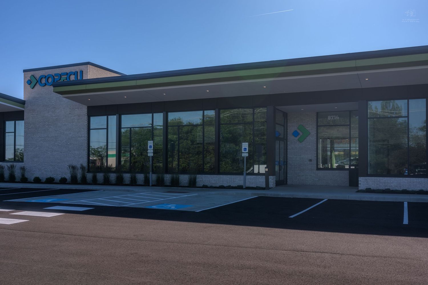 Modern Optum healthcare clinic exterior with large glass windows, stone facade, and accessible parking spaces on a sunny day.
