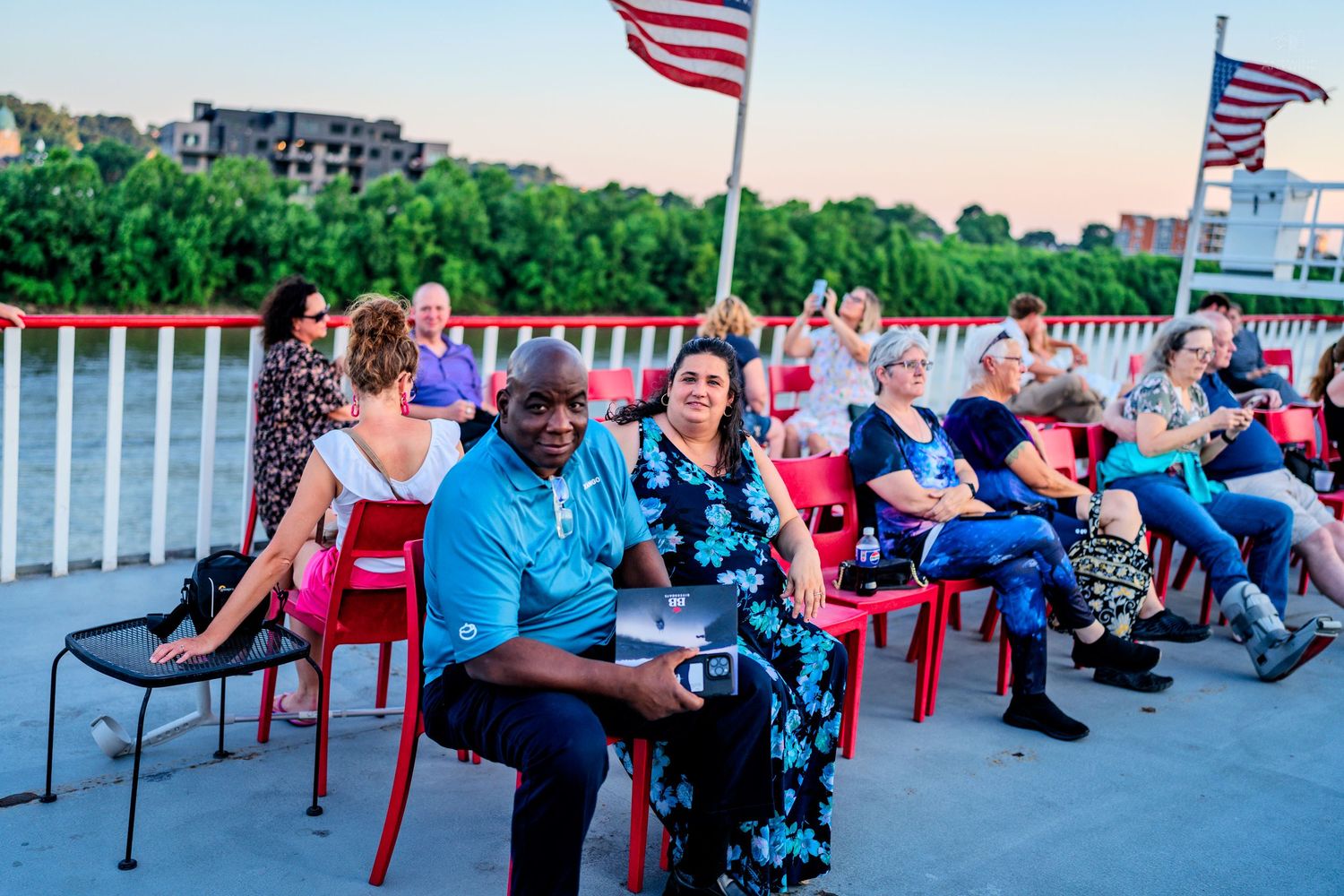 Diverse group of guests seated on boat deck with American flags during an outdoor evening event.