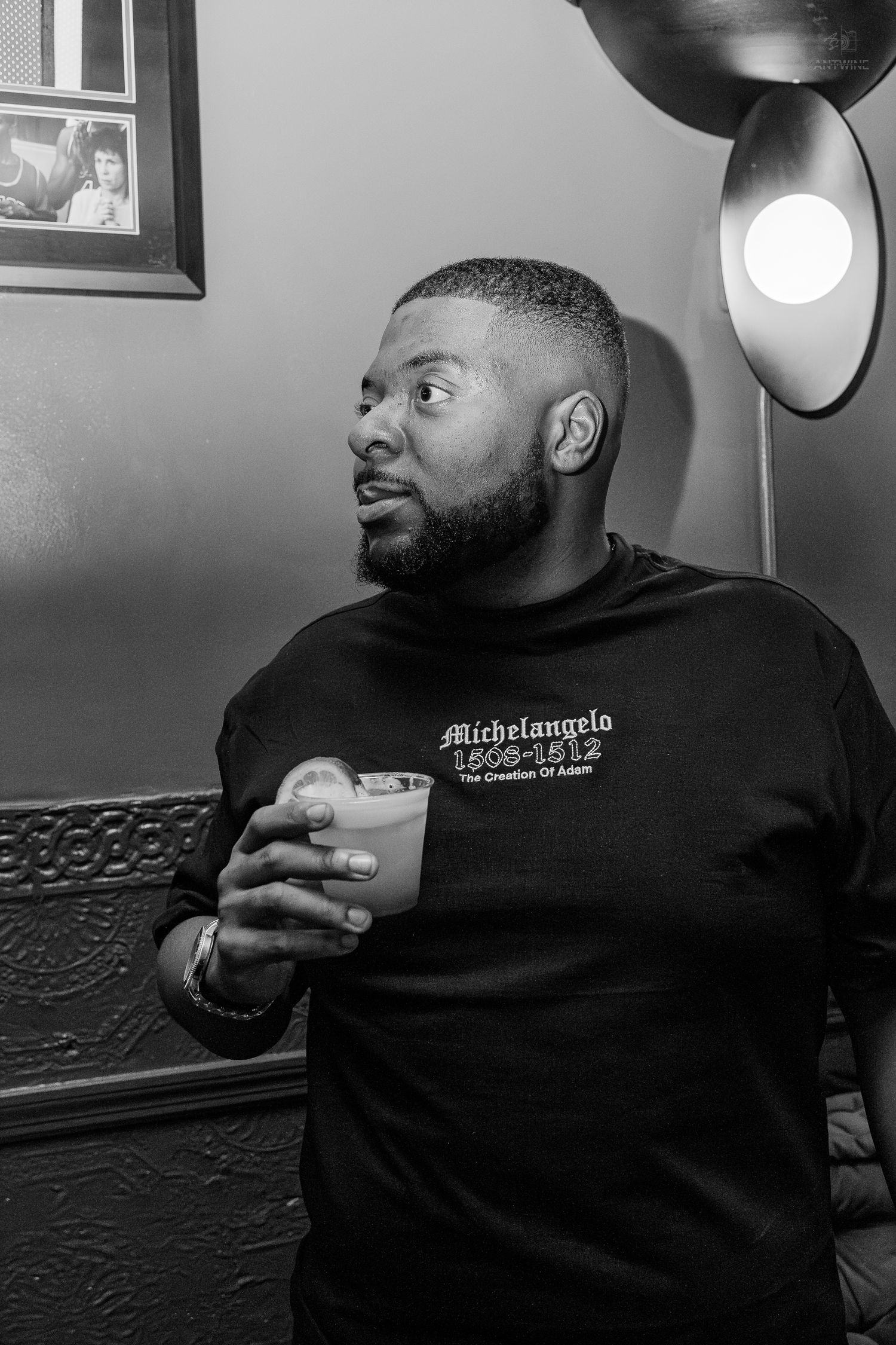 Man in Michelangelo graphic sweatshirt holding a drink in black and white bar photo.