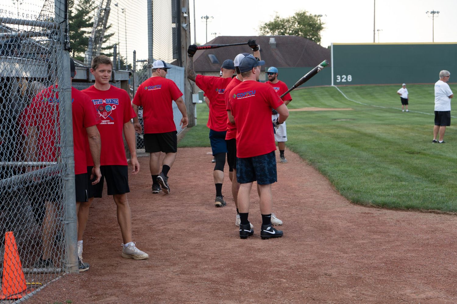 Baseball players in red team shirts walk along the warning track of a baseball field during practice.