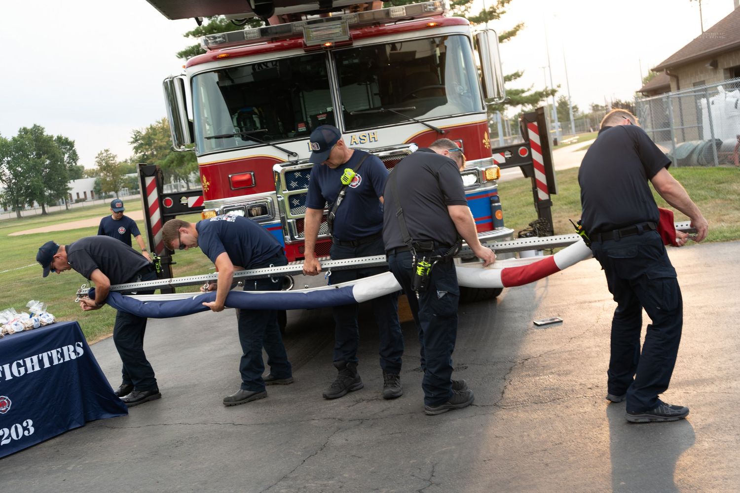 Firefighters assemble rescue equipment near red fire truck at outdoor community event.