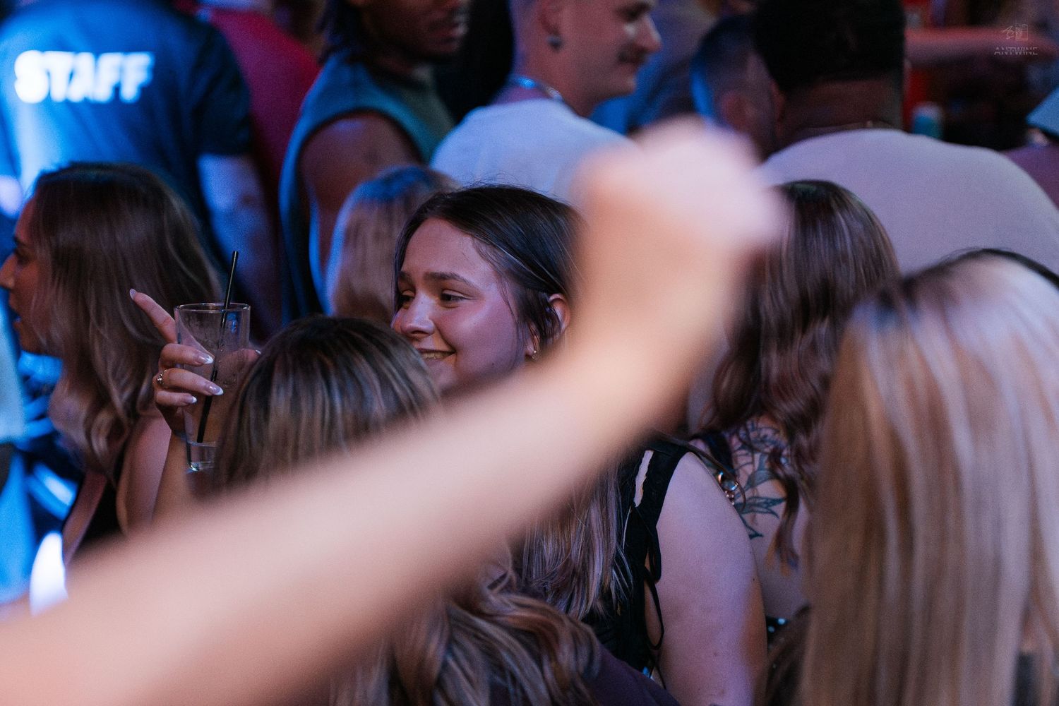A smiling woman holds a drink while surrounded by friends at a lively bar event.