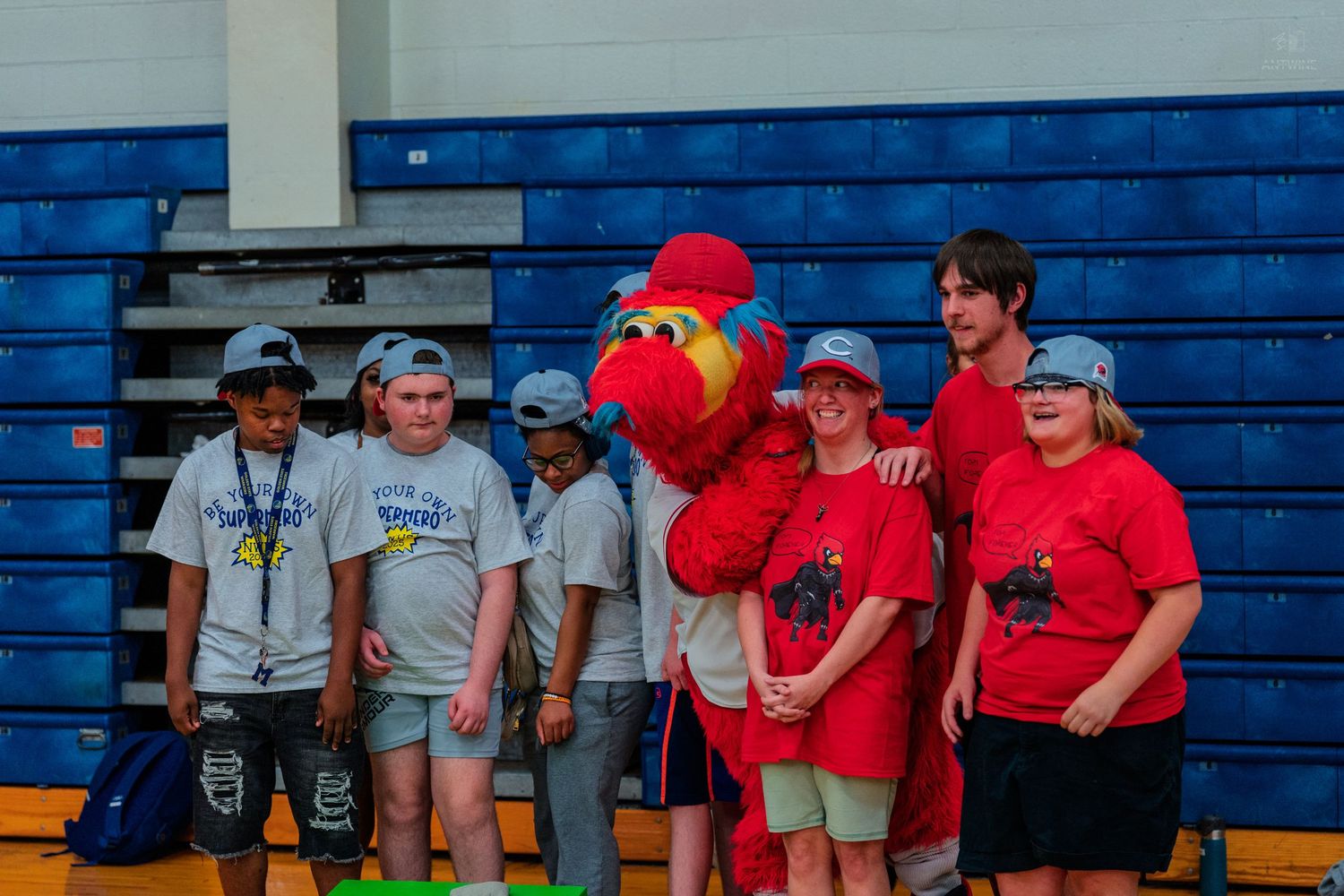 Cincinnati Reds mascot Mr. Red poses with a group of young participants in red shirts in a gymnasium.